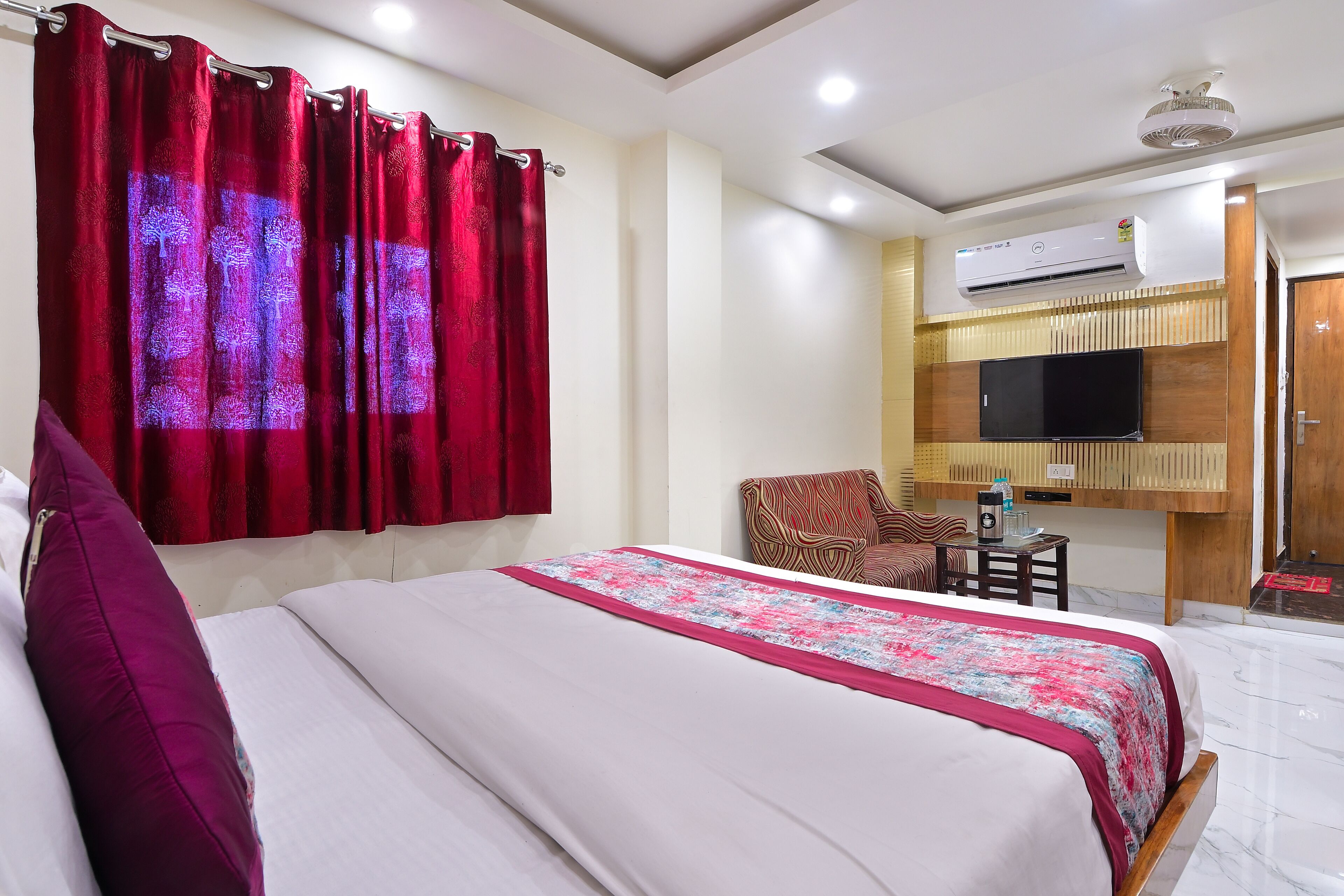 A hotel room with a bed, a TV, an air conditioner, and a chair.