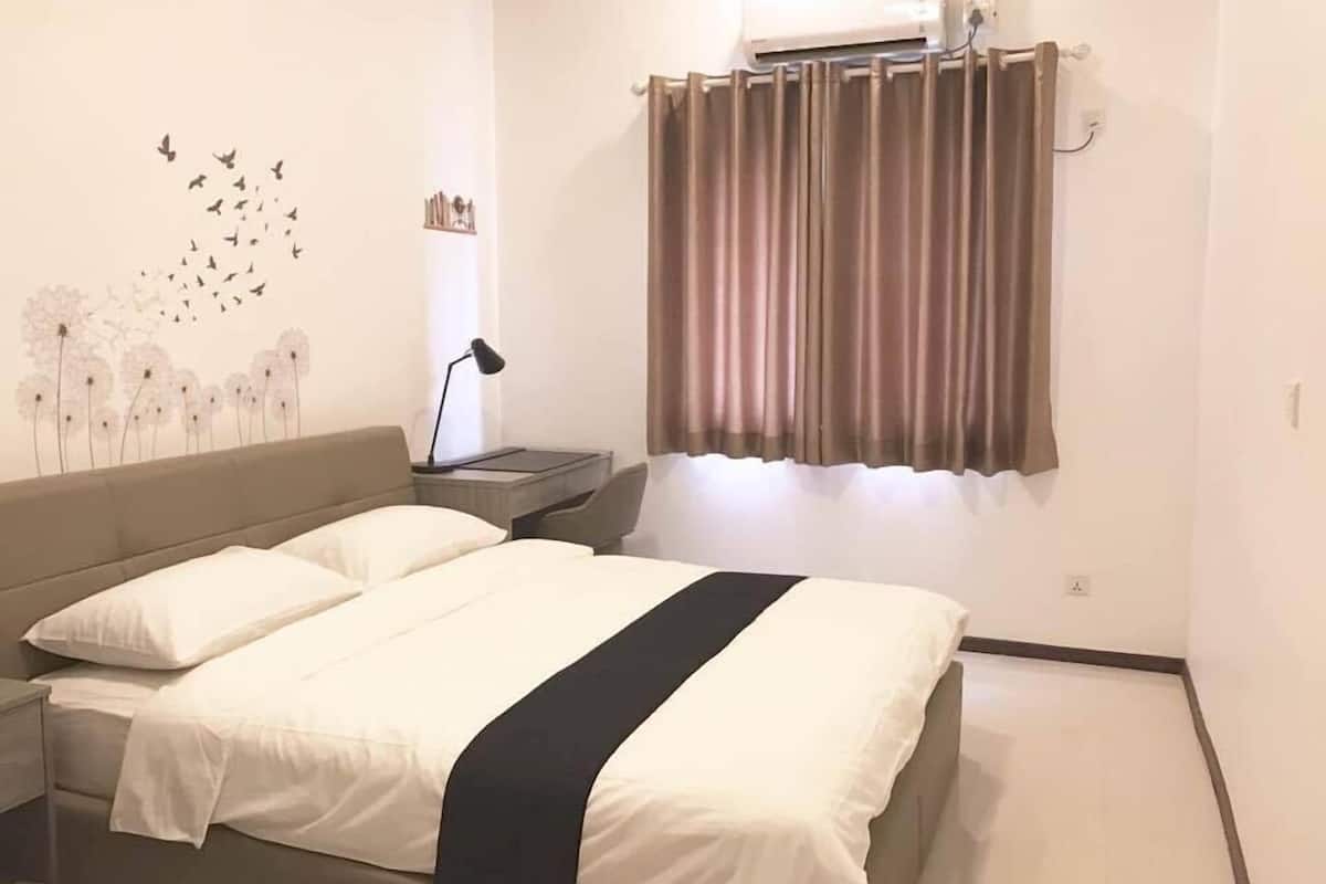 A bedroom with a bed, a nightstand, a lamp, a window with curtains, and a wall decoration of birds and flowers.