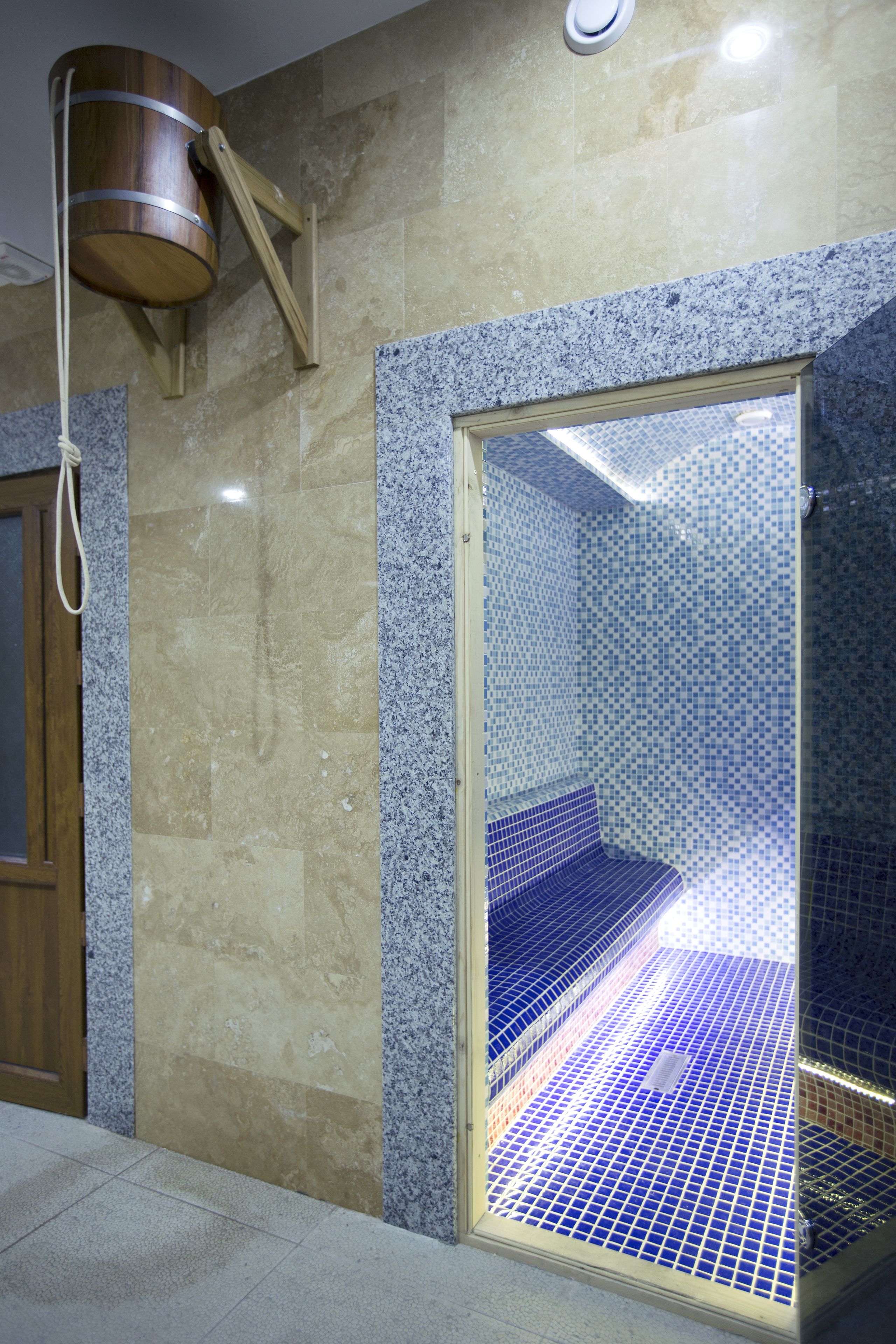 Ein Badezimmer mit Duschbereich, der blaue Mosaikfliesen und einen Holzeimer zeigt.