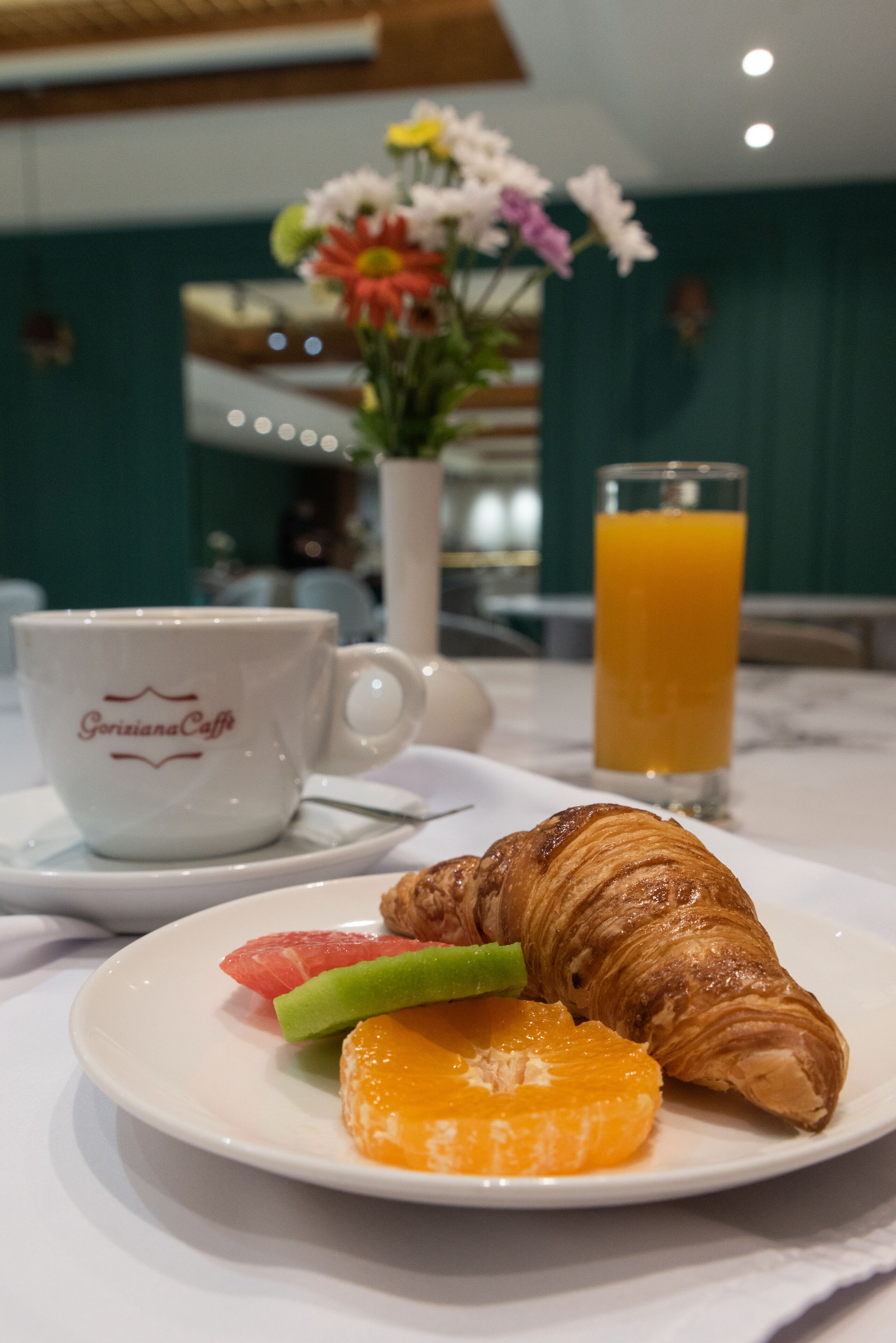 A breakfast setting with a croissant, orange slice, and grapefruit on a plate, a coffee cup, and a glass of orange juice.