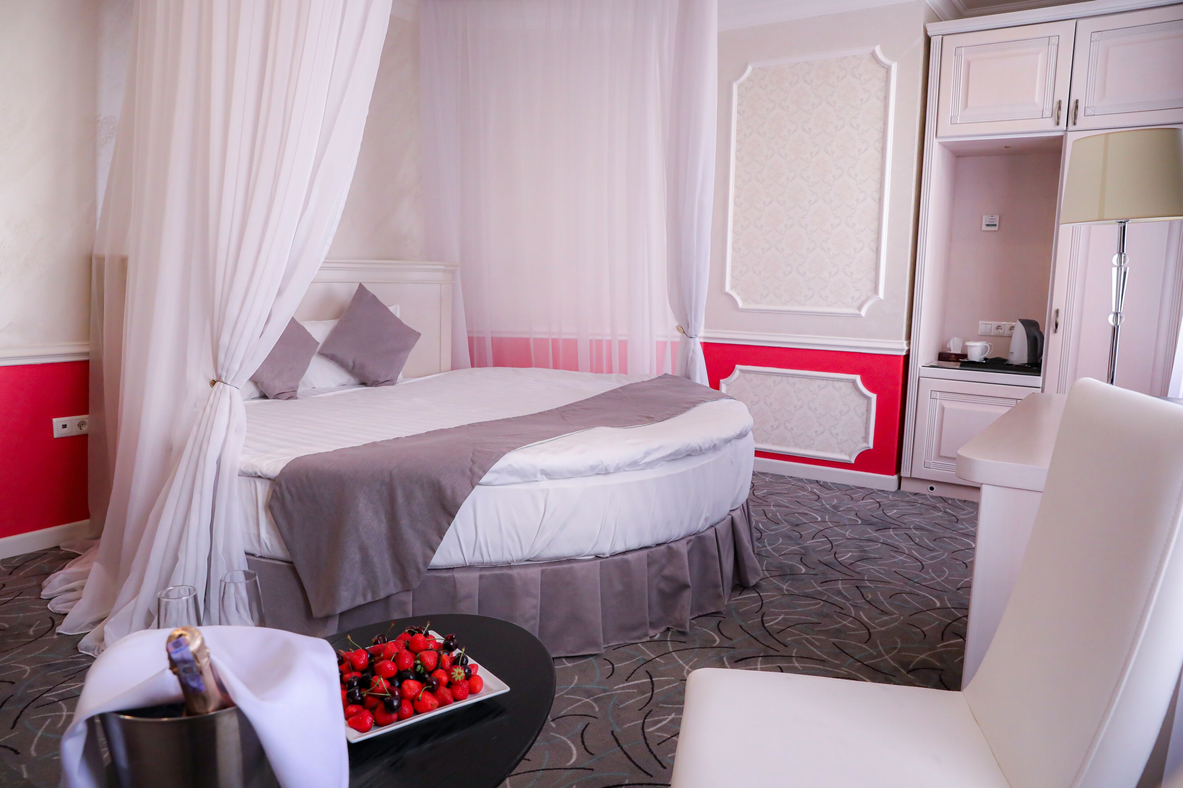 A bedroom with a bed, a bedside table with a bottle, and a bowl of fruit.