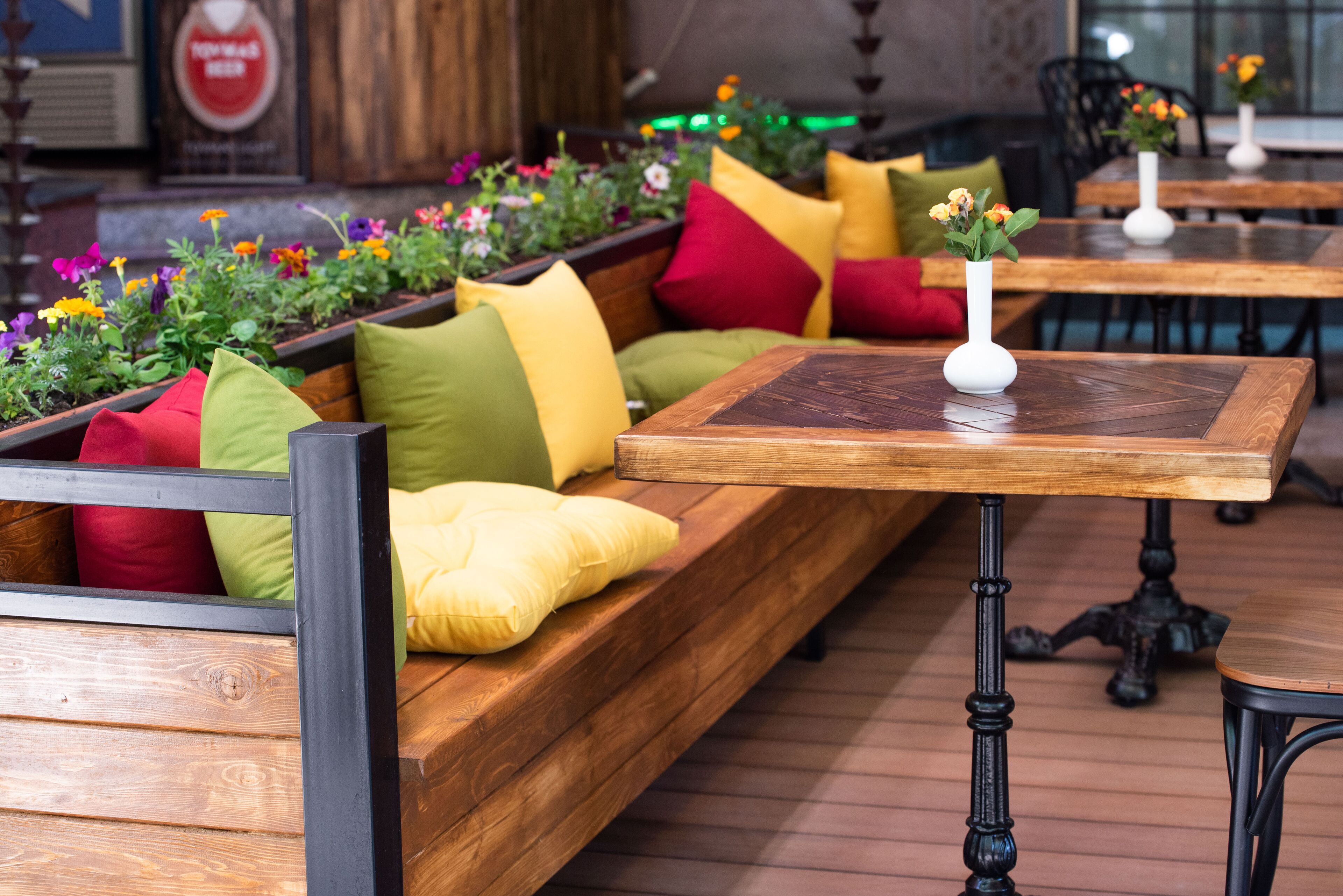 A wooden bench with colorful cushions and a small table with a vase of flowers.