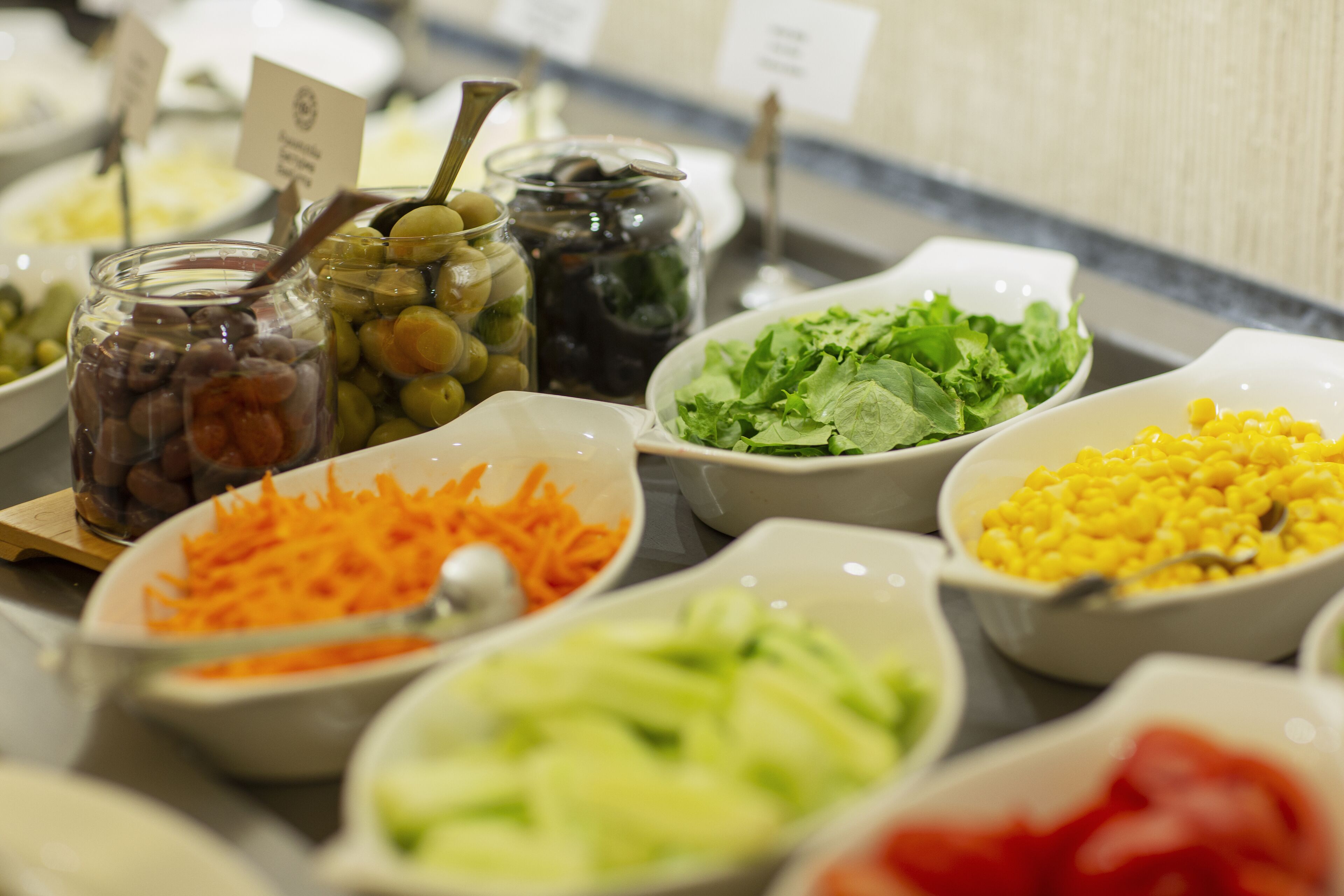 Een buffet met diverse soorten eten, zoals olijven, wortels, sla, maïs en rode saus.