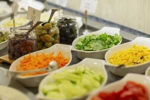 Een buffet met diverse soorten eten, zoals olijven, wortels, sla, maïs en rode saus.