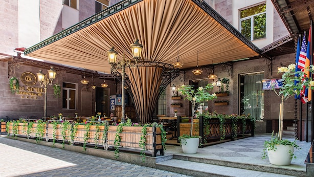 An outdoor seating area with a covered patio, potted plants, and a sign for 'Hotel Solruss'.