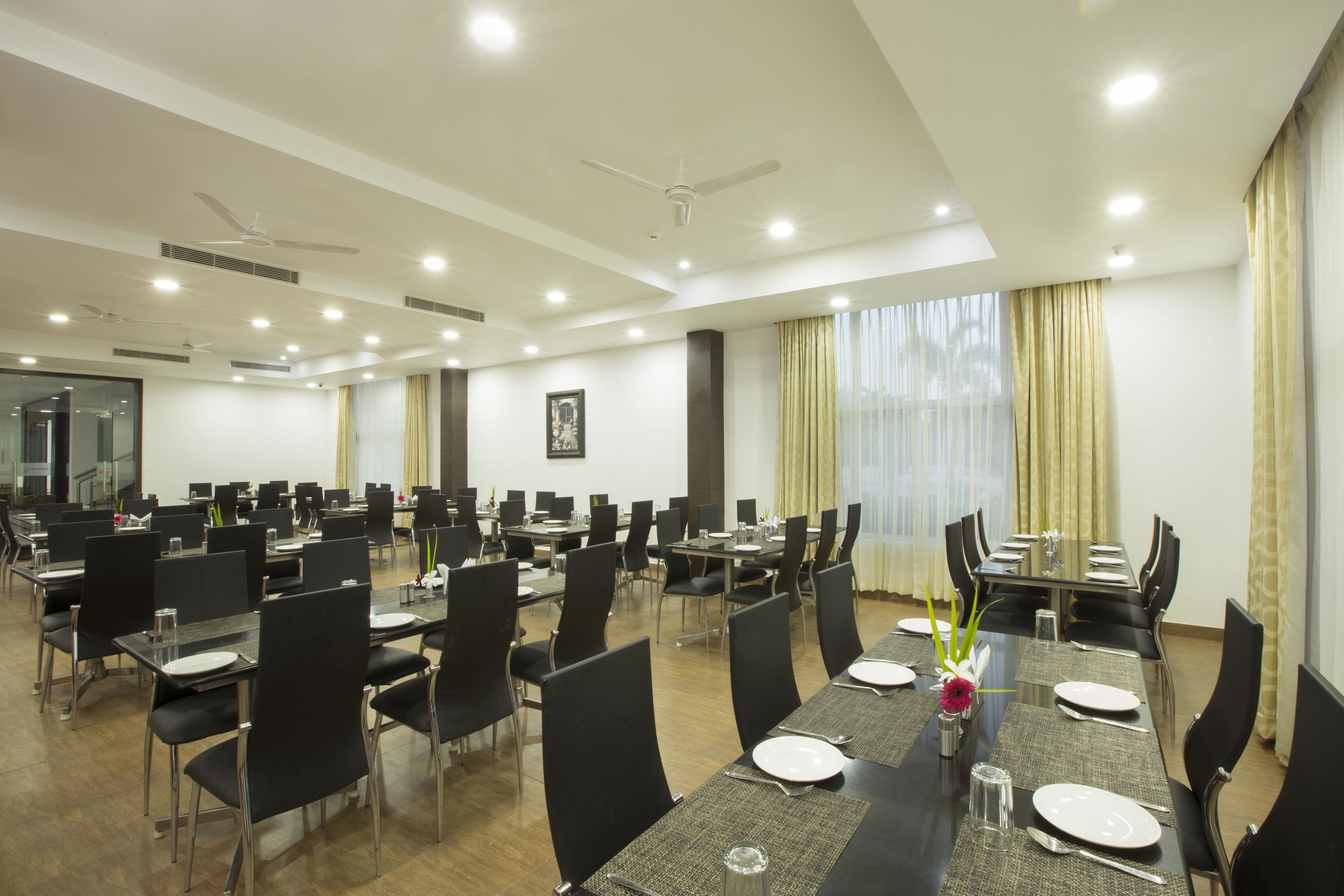 A conference room with multiple tables and chairs, equipped with ceiling fans and recessed lighting.