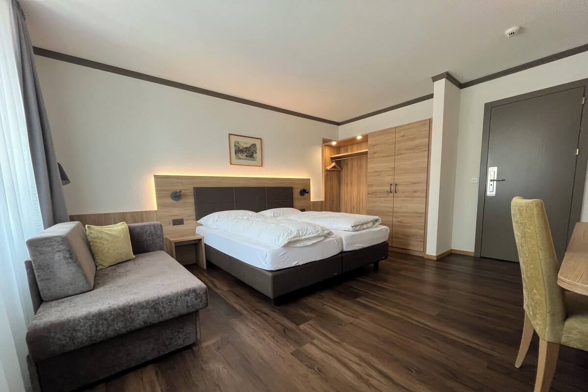 Una habitación de hotel con cama doble, sofá, sillón, armario y escritorio.