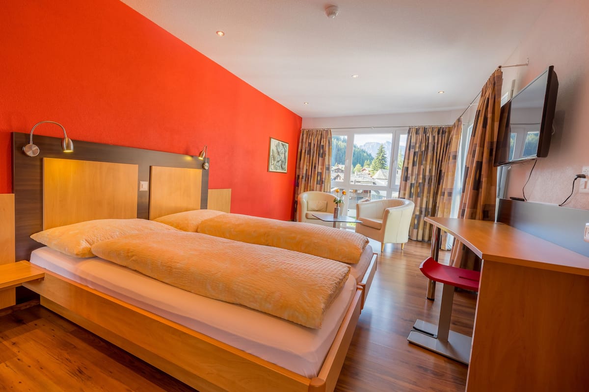 Habitación de hotel con una cama grande, cabecera de madera, un escritorio con silla, televisión y vistas al exterior.