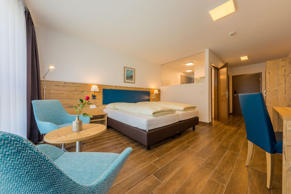 Una habitación de hotel con una cama, dos sillones, una mesita y un cabecero de madera.