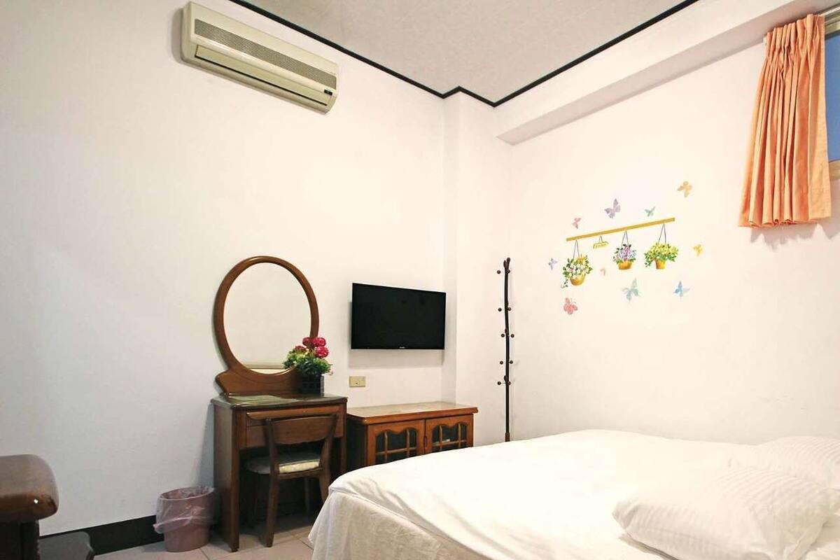 A bedroom with a bed, a dresser with a mirror, a television, and a wall decoration.