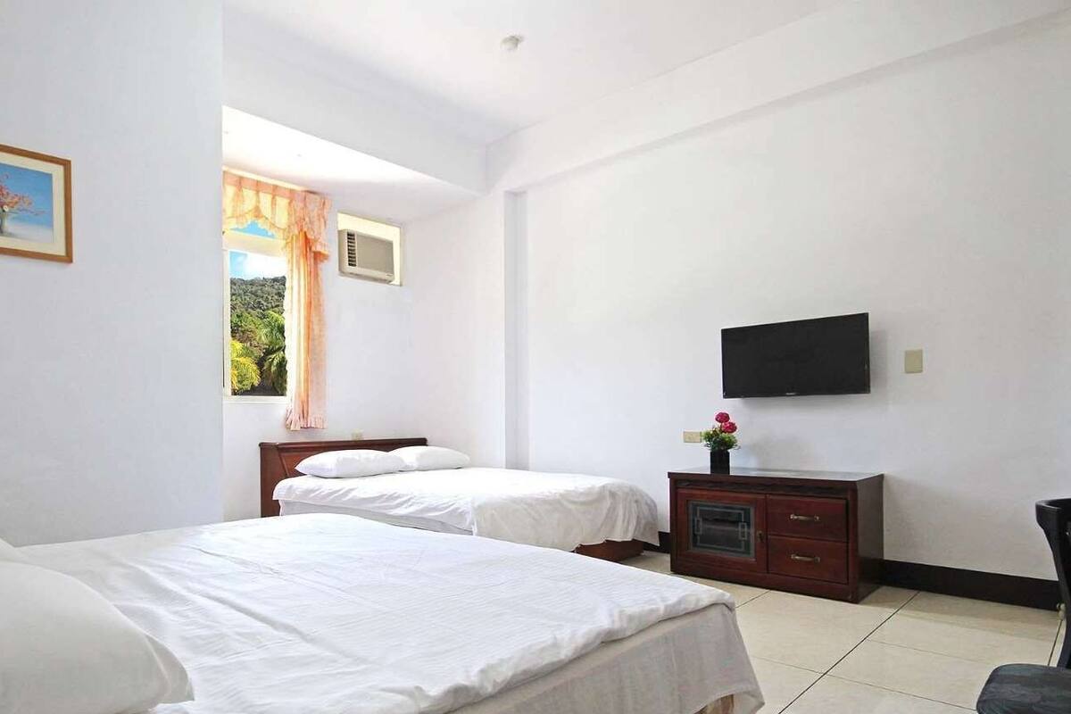 A hotel room with two beds, a TV, a window with curtains, and a painting on the wall.