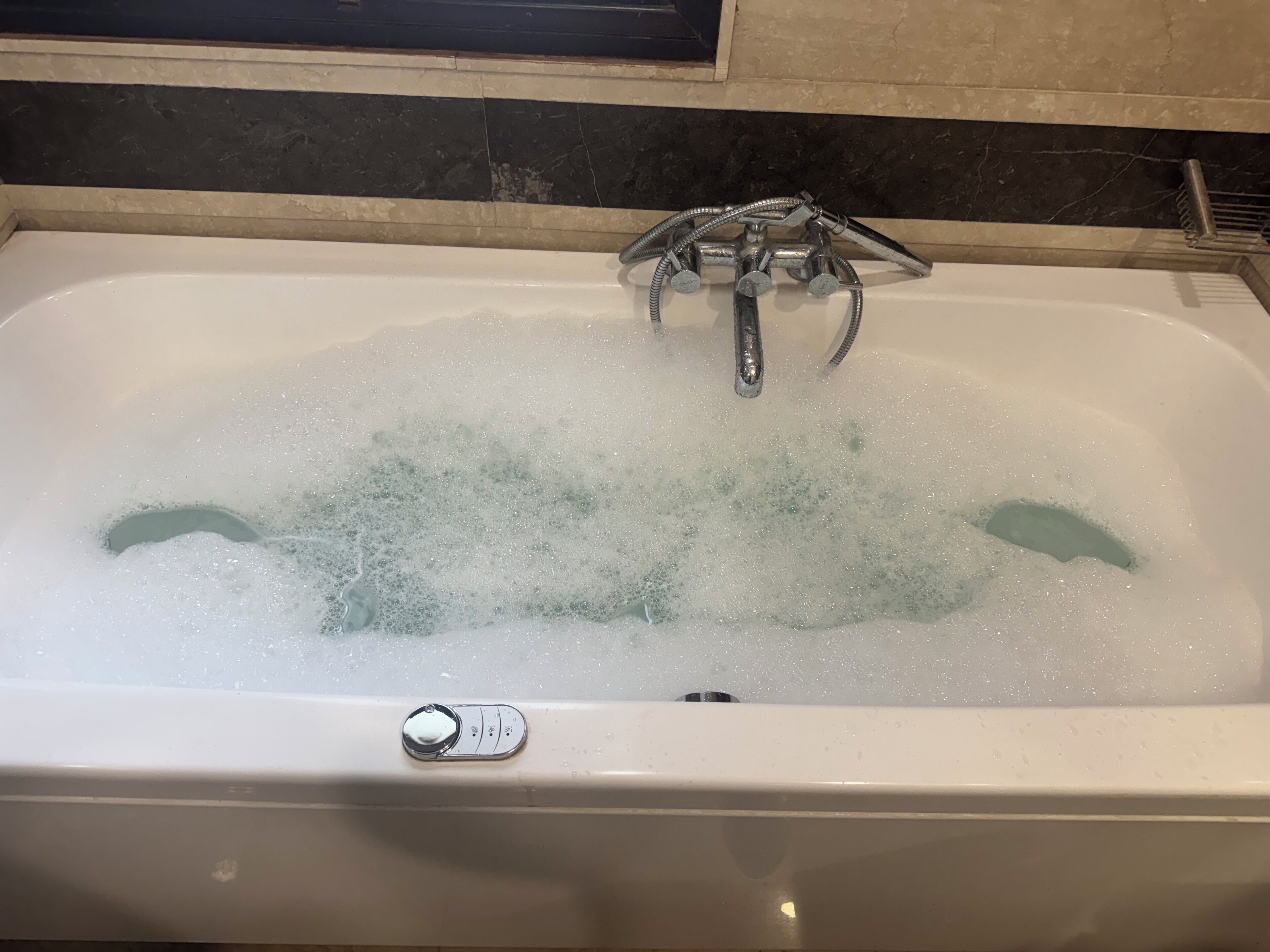 A bathtub filled with bubbles, a faucet, and a control panel.