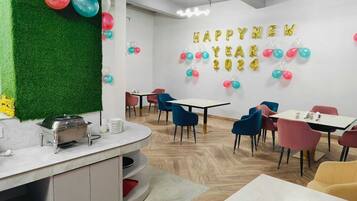 Un comedor moderno con mesas y sillas redondas, una estación de buffet y una pared decorada con globos y el texto 'HAPPY NEW YEAR 2024'.