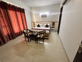 Une chambre d’hôtel comprenant un lit, un bureau, deux chaises, une table de chevet et un climatiseur fixé au mur.