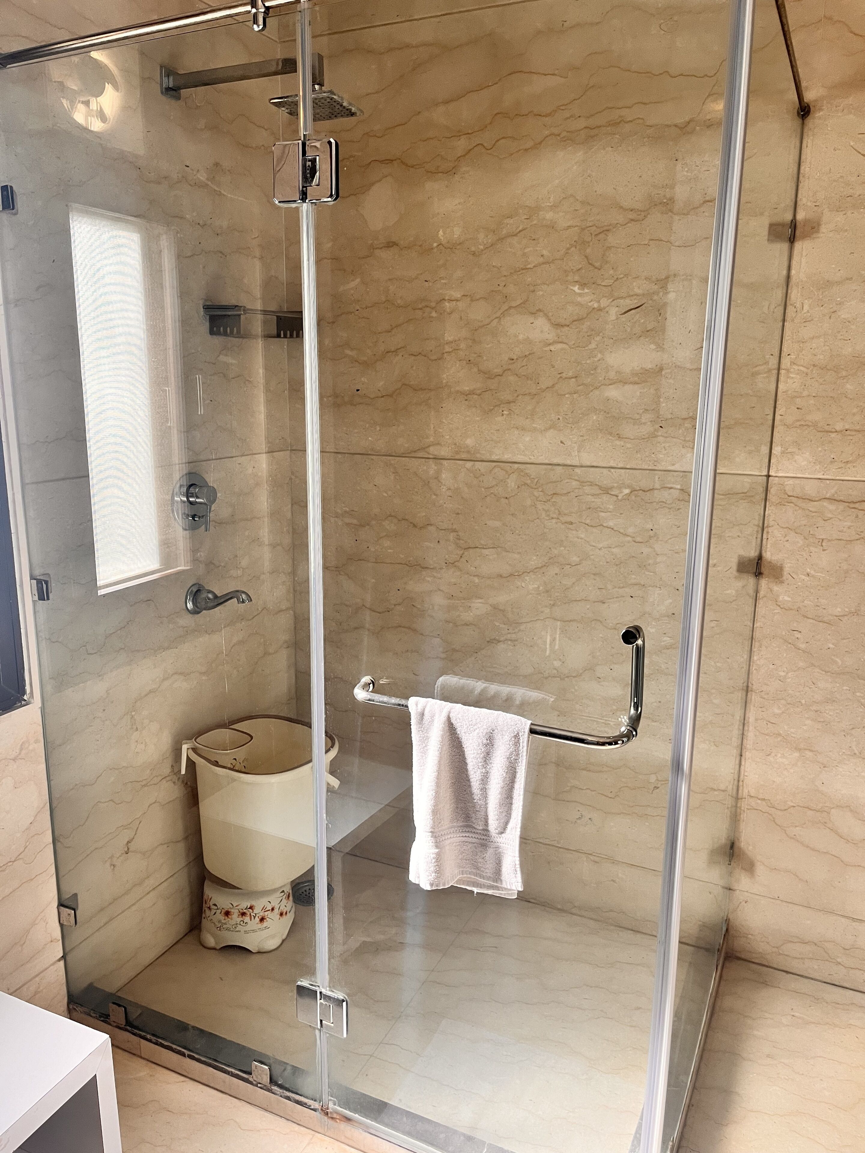 A glass-enclosed shower with a glass door, a towel rack, and a toilet with a floral design.