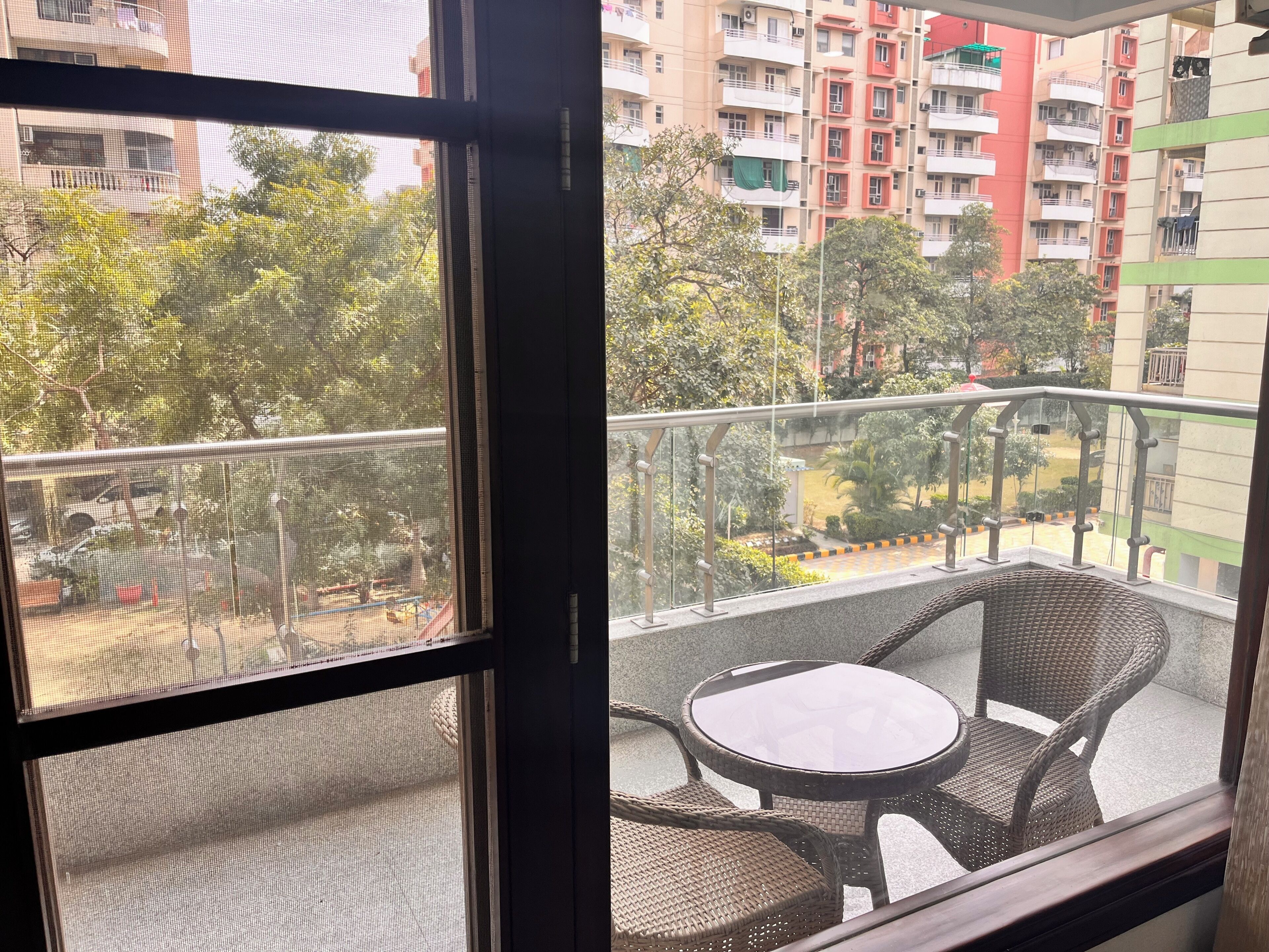 A balcony with wicker furniture and a view of a residential area with multi-story buildings.