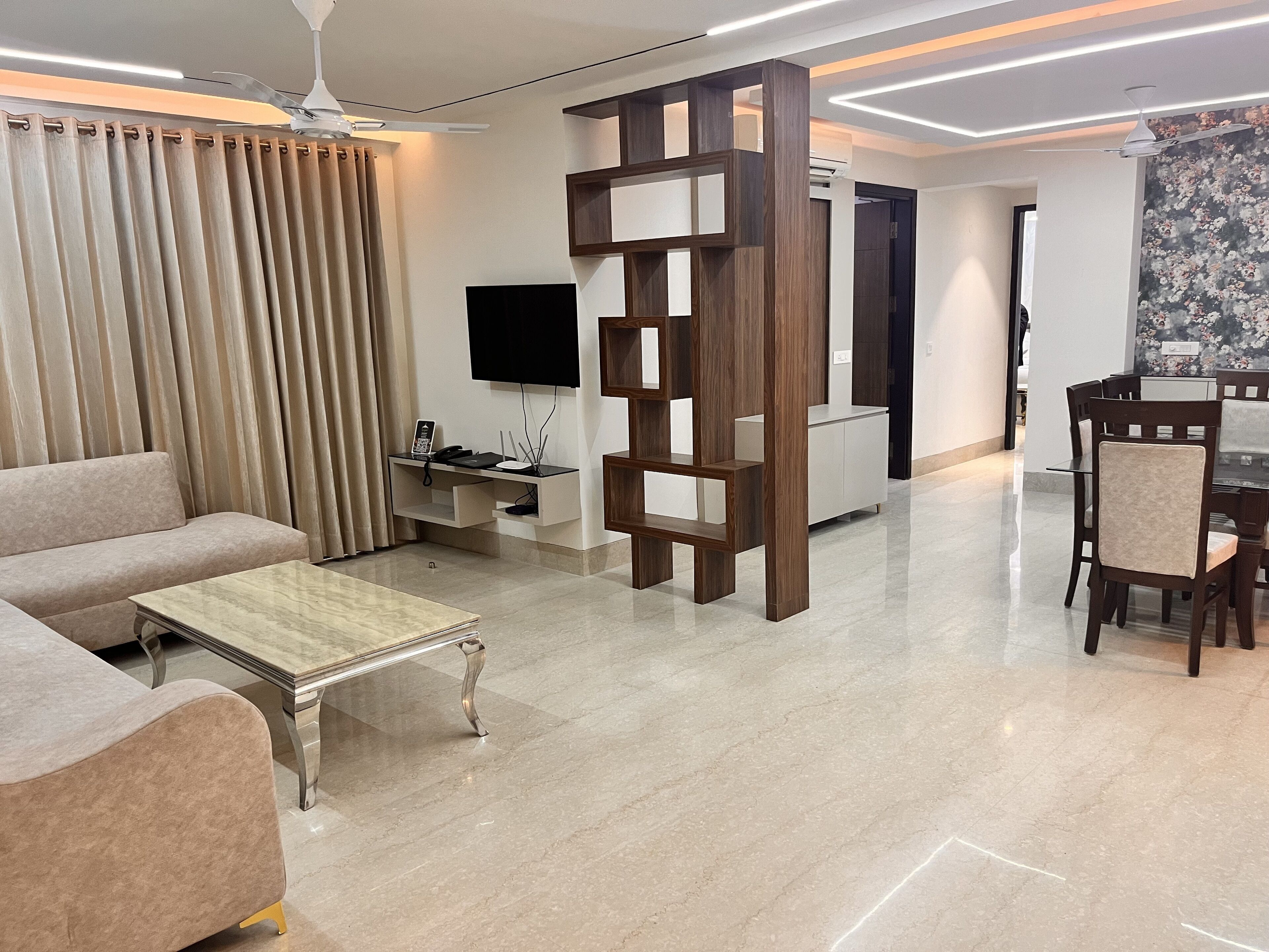 A modern living room with a sofa, coffee table, TV, and a dining area with chairs and a table.