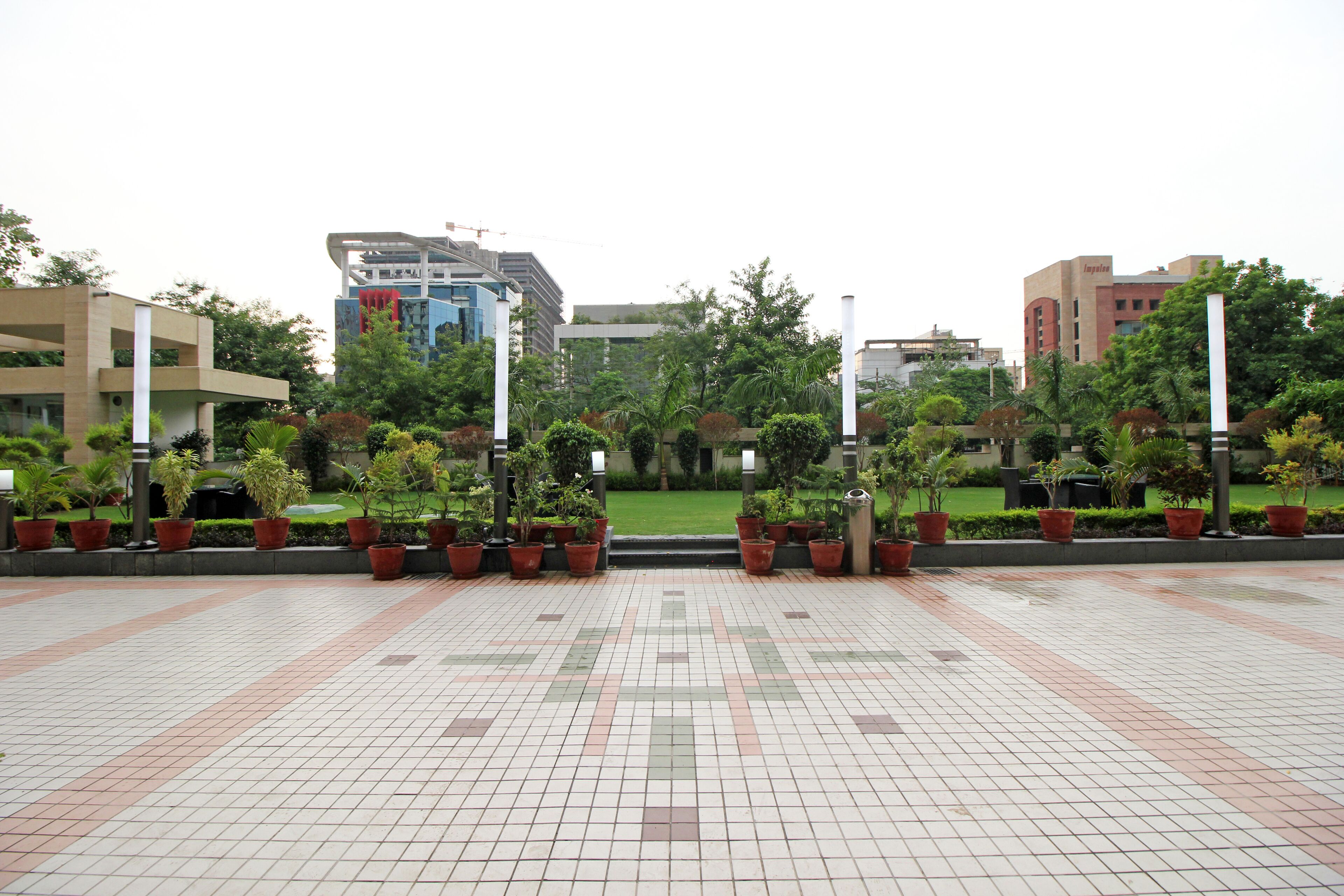 A spacious outdoor area with tiled flooring and potted plants arranged in rows.