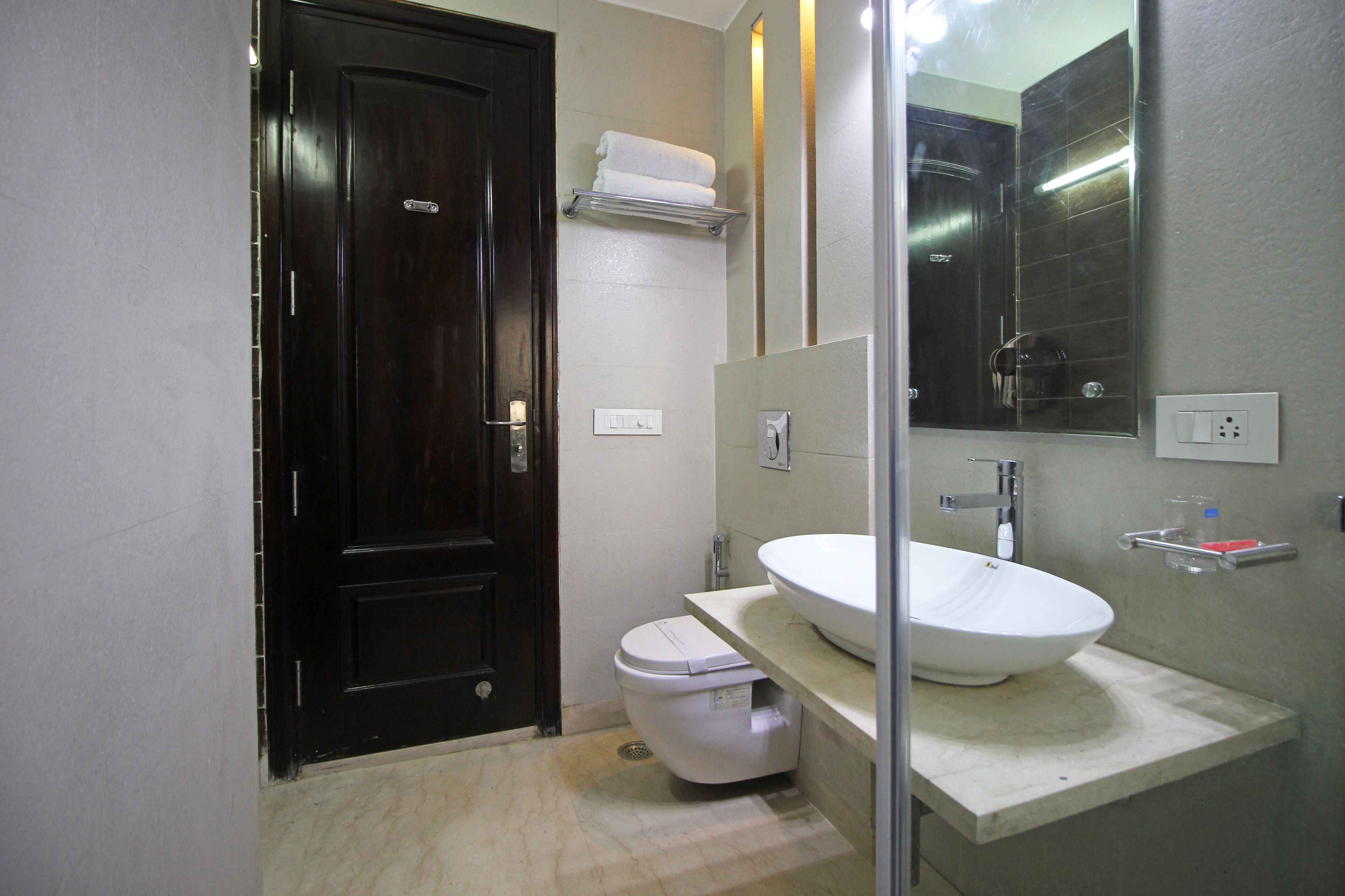 A bathroom with a dark wooden door, a white toilet, a large mirror, and a white sink with a countertop.