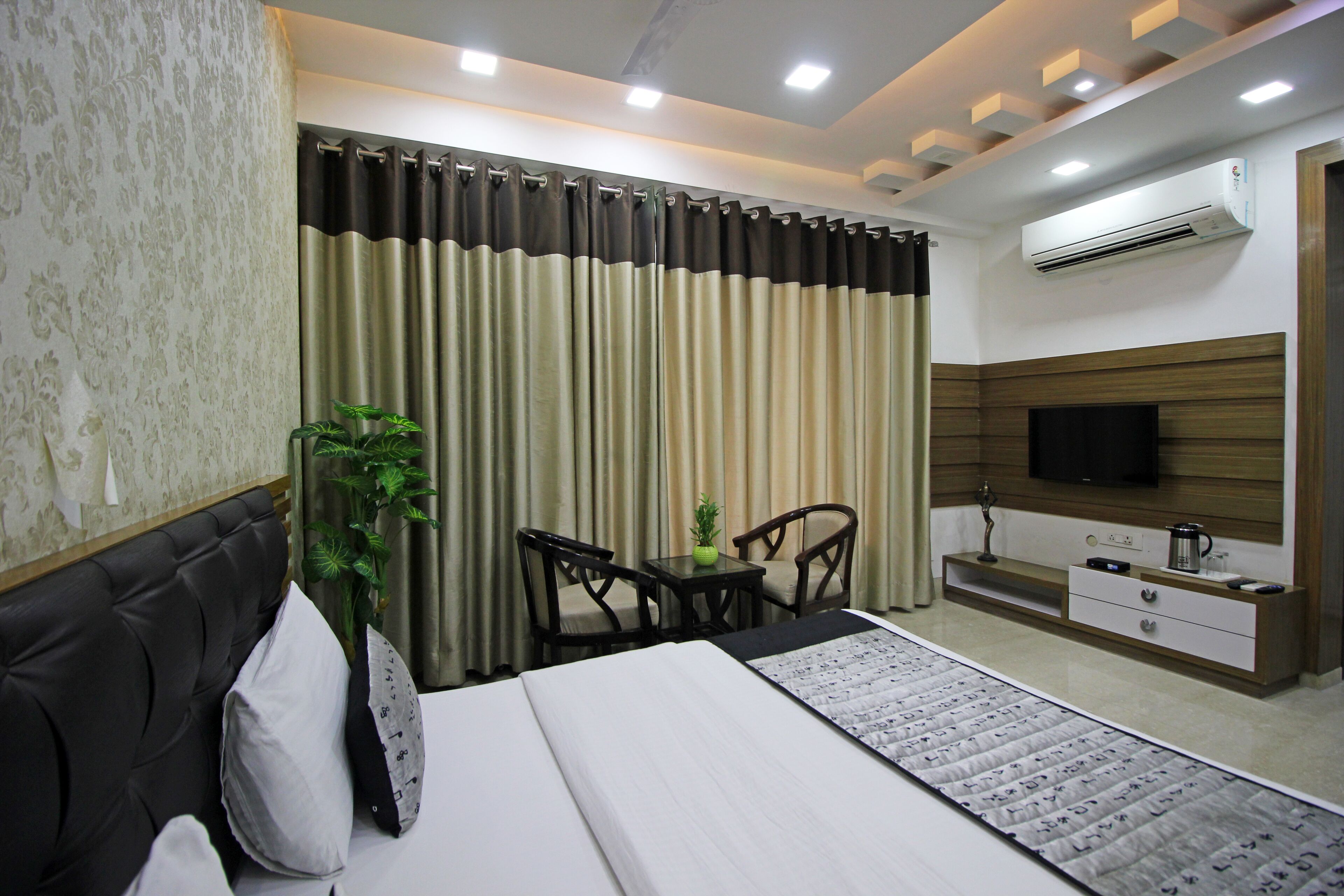 Una habitación de hotel moderna con cama, televisor, una pequeña mesa con sillas y una planta en maceta.