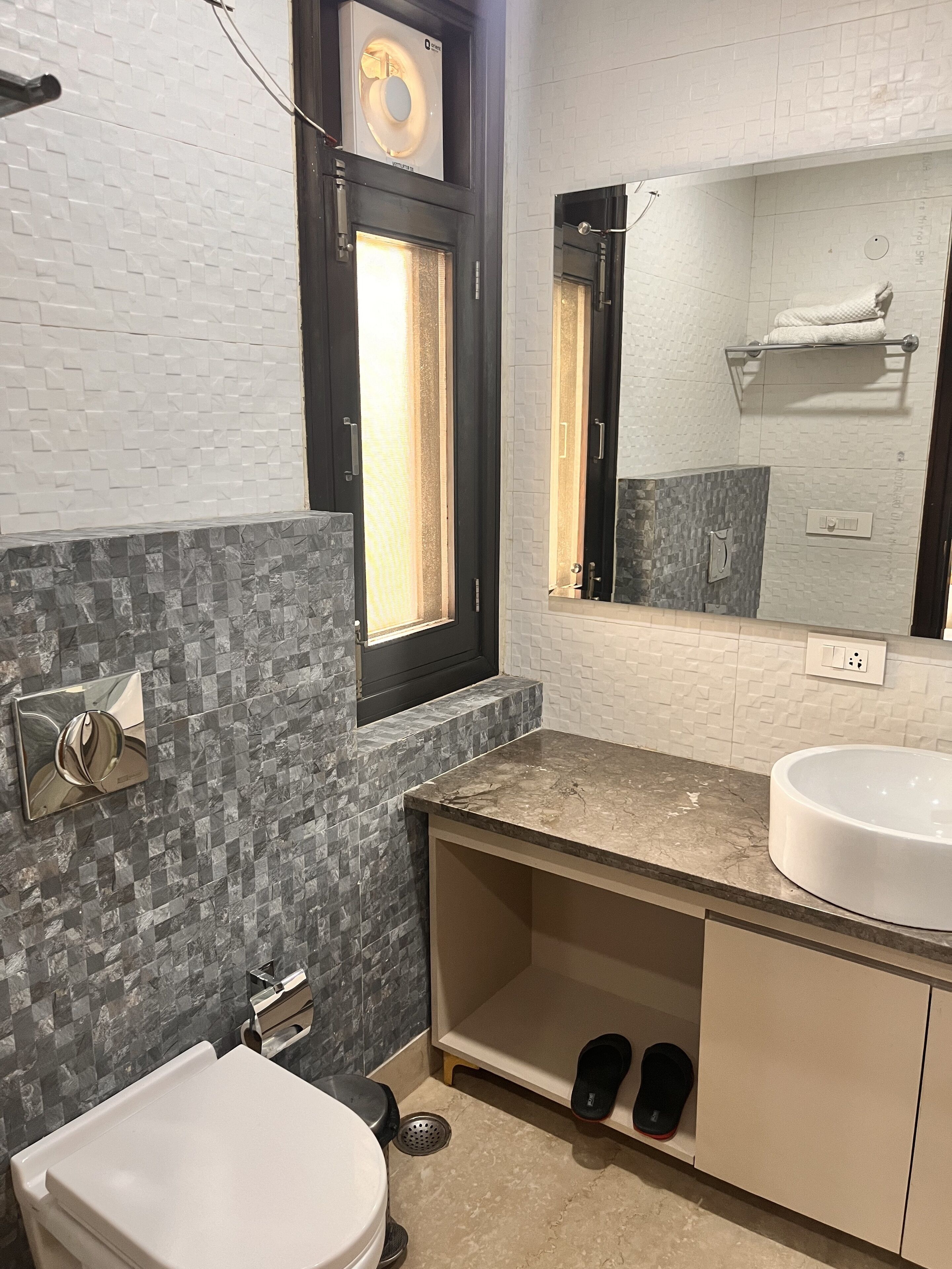 A bathroom with a white toilet, a sink with a marble countertop, a mirror above the sink, and a window with a towel rack.