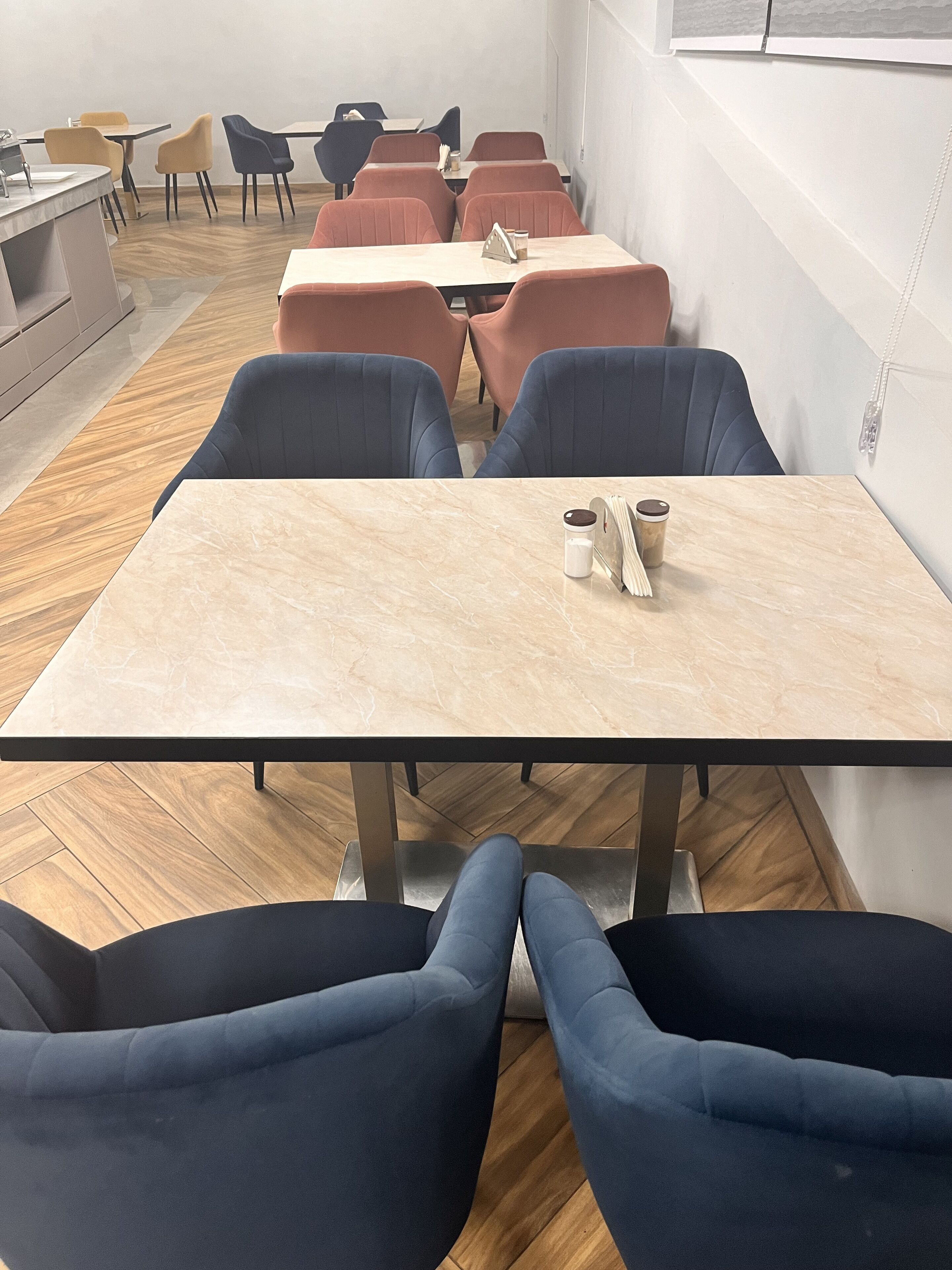 A modern meeting room with a marble table, blue and red chairs, and a wooden floor.