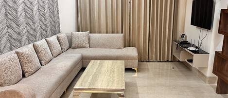 A modern living room with a sectional sofa, a wooden coffee table, a TV mounted on the wall, and a herringbone-patterned wall.
