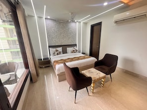 Habitación de hotel con cama, dos sillas, mesita de noche y ventana con vistas al exterior.