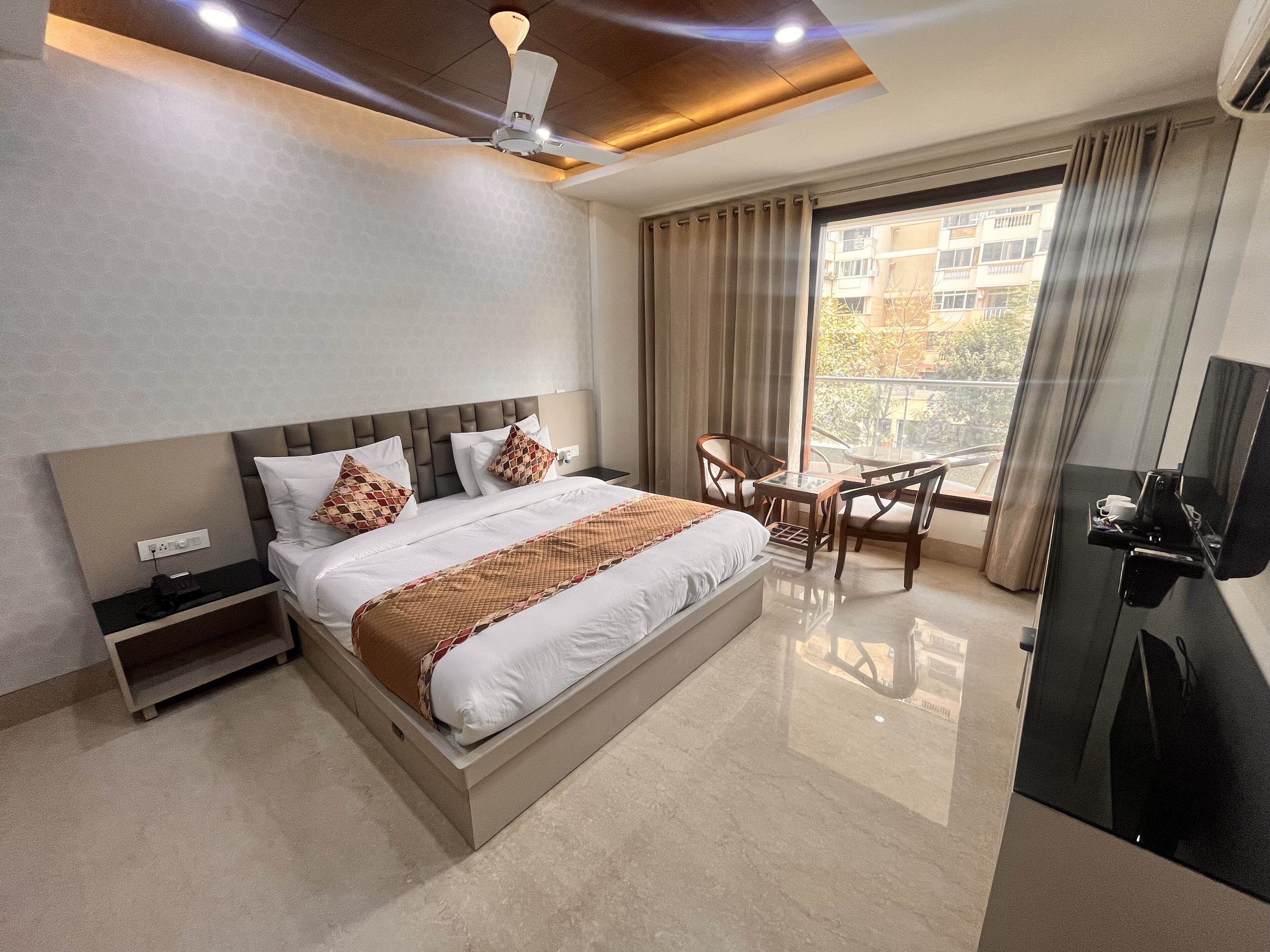 Une chambre d’hôtel moderne dotée d’un grand lit, d’un bureau avec une chaise, d’un ventilateur de plafond et offrant une vue sur l’extérieur.