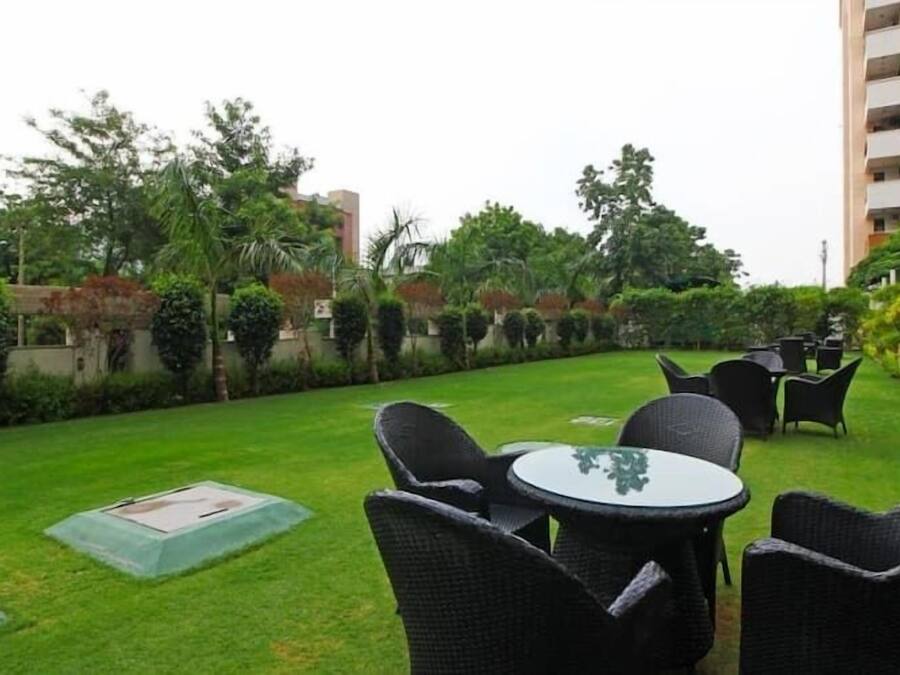 Un patio con mobiliario exterior, un césped cuidado y abundante vegetación.