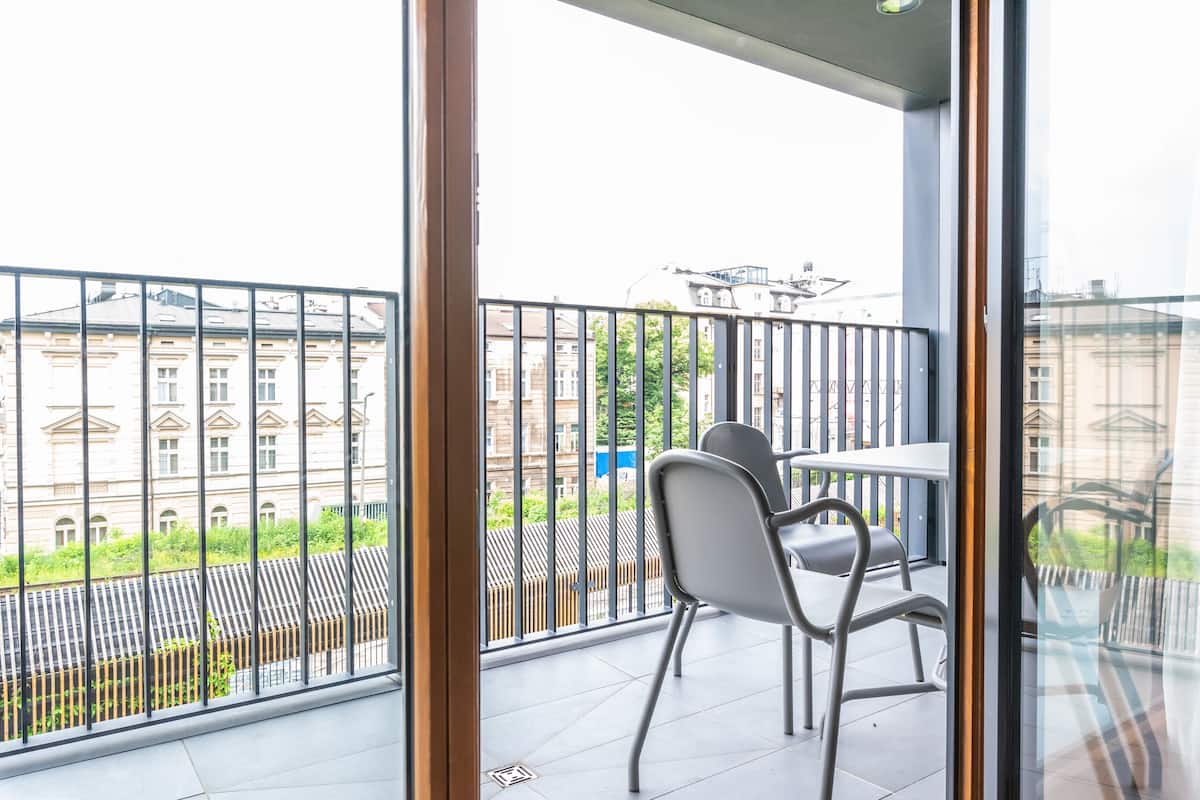 Een balkon met een tafel en stoelen, uitzicht op gebouwen en een metalen hek.