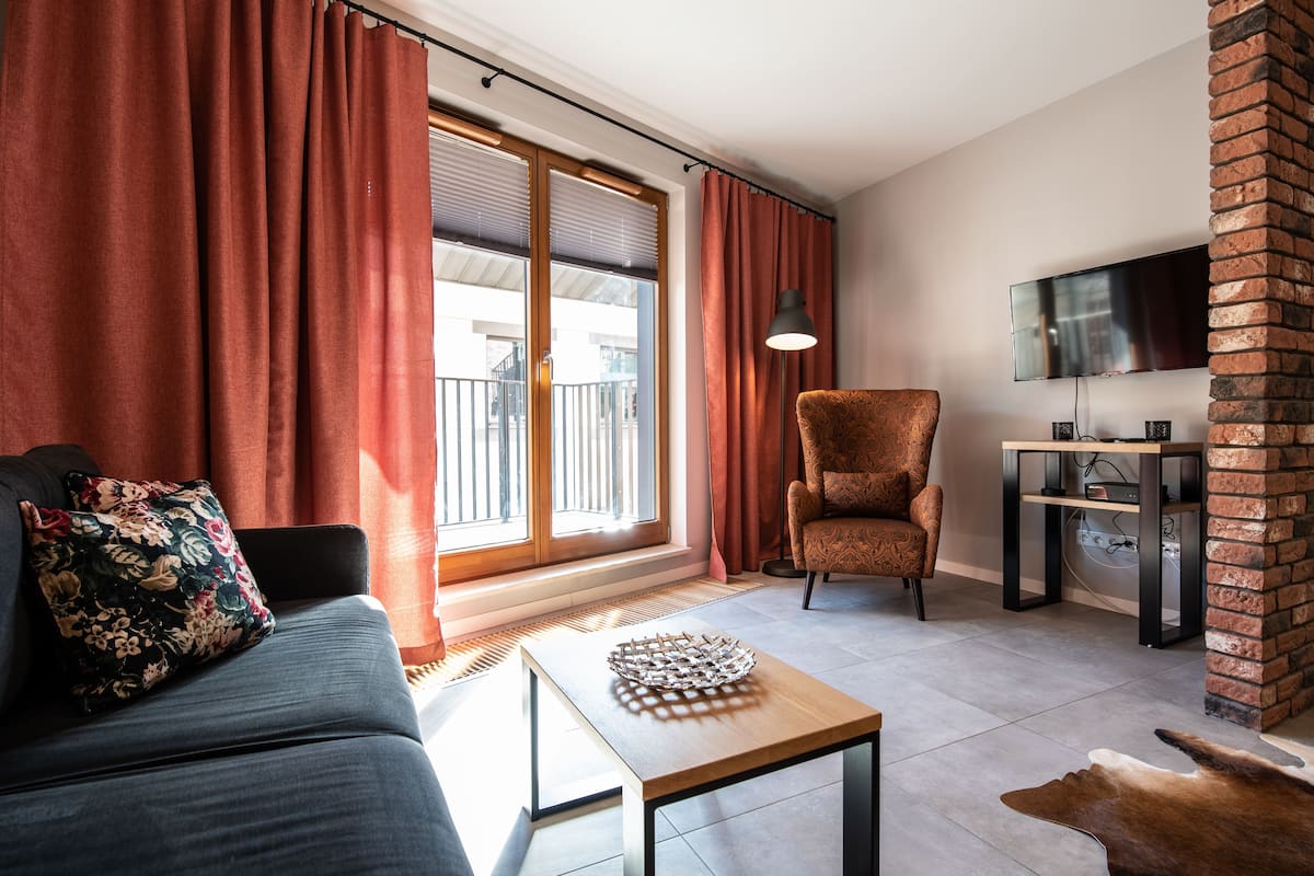 Een moderne woonkamer met een bank, een fauteuil met een patroon, een salontafel en een televisie bevestigd aan een bakstenen muur.