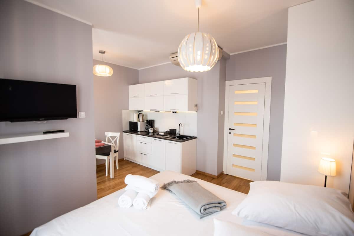 Een moderne hotelkamer met een bed, een aan de muur bevestigde televisie, een kitchenette en een deur met verlicht paneel.