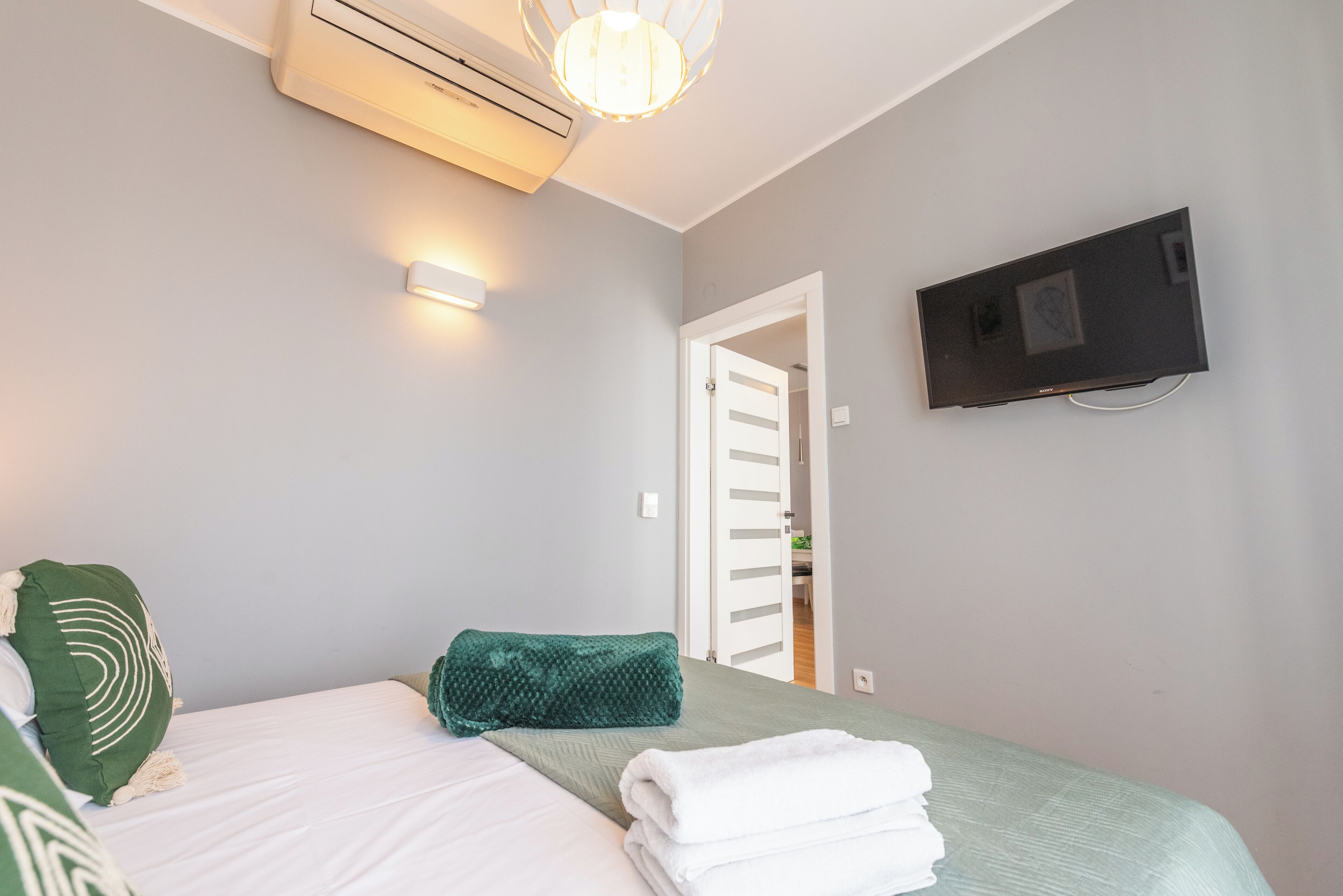 A bedroom with a bed, pillows, a TV, and an air conditioning unit.