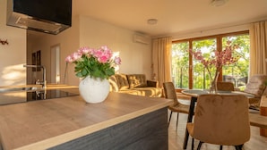 A modern kitchen with a built-in stove, a dining area with a round table and chairs, a sofa, and a large window with a view of greenery. - City Lights Apartments (Kraków)