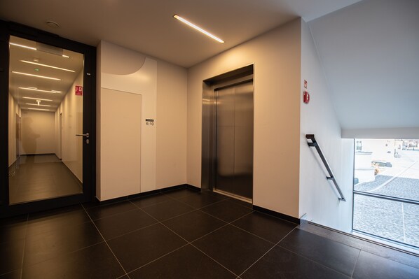 A modern hallway with an elevator, a door marked 6-10, and a glass door leading outside.
