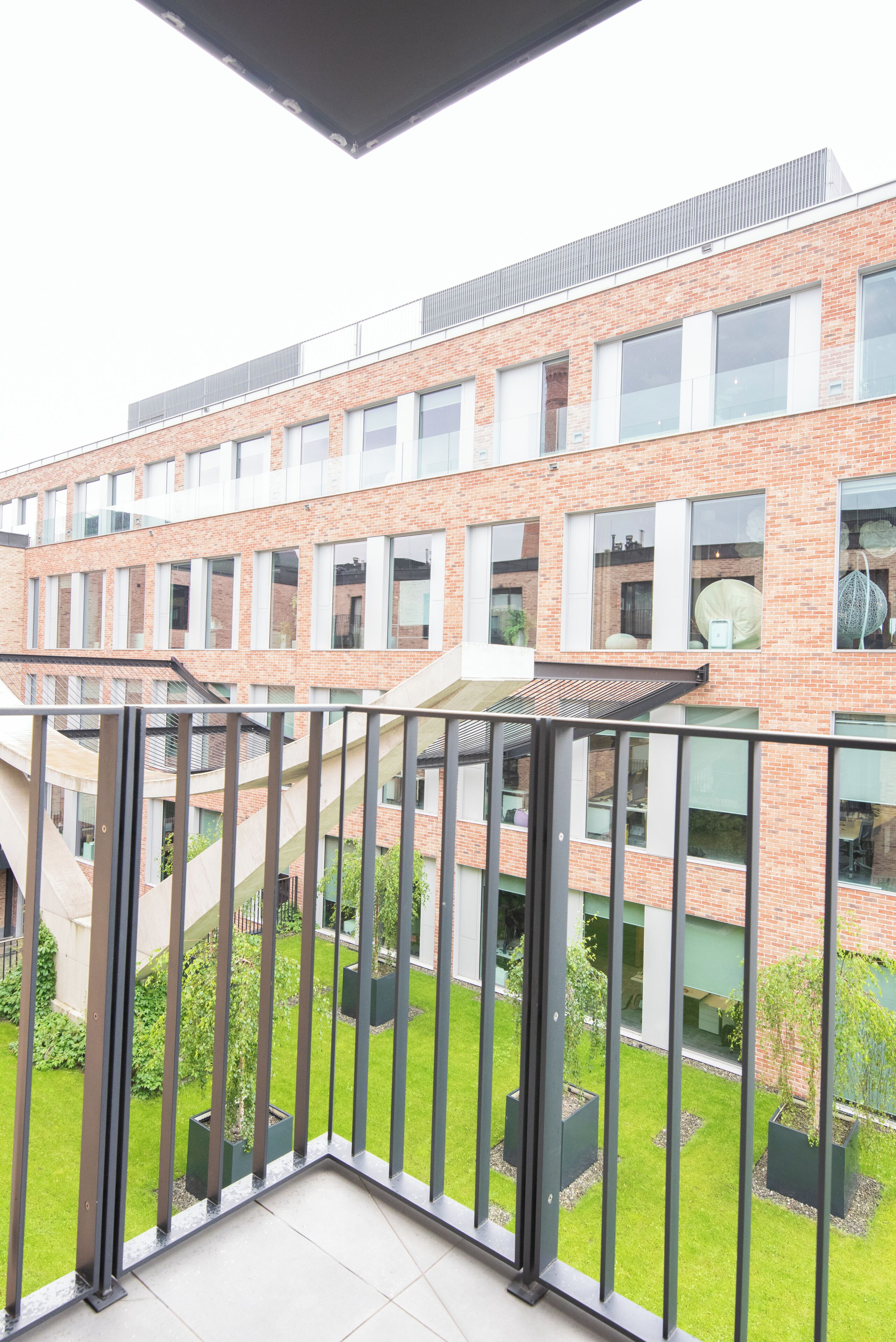 A modern building with a brick facade, large windows, and a balcony with a metal railing.