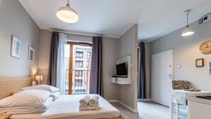 A modern hotel room with a wooden bed, a TV mounted on the wall, and a view of the city through the window. - City Lights Apartments (Kraków)