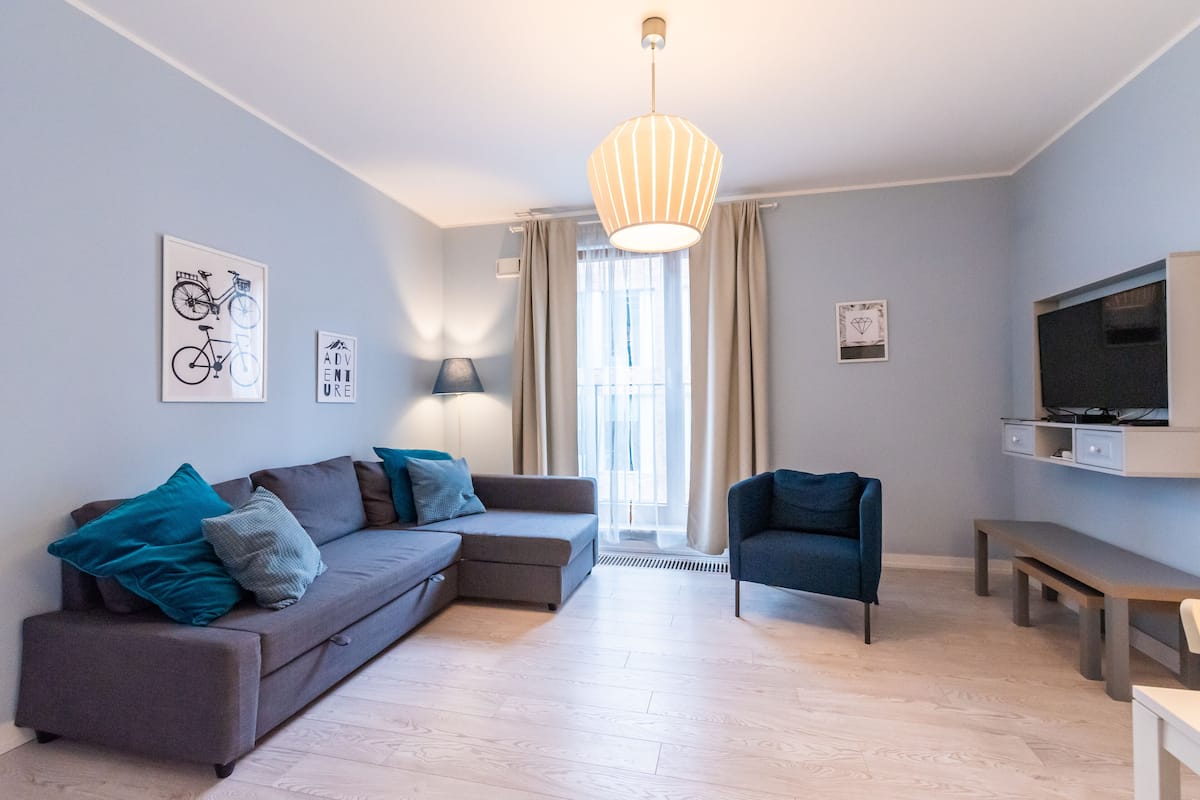 Een moderne woonkamer met een hoekbank, een fauteuil, een bankje en een televisie op een inbouwplank.