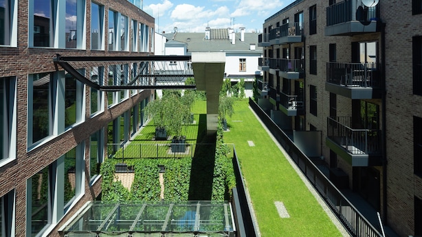 A modern building with multiple floors, large windows, and a central courtyard with grass and plants. - City Lights Apartments (Kraków)