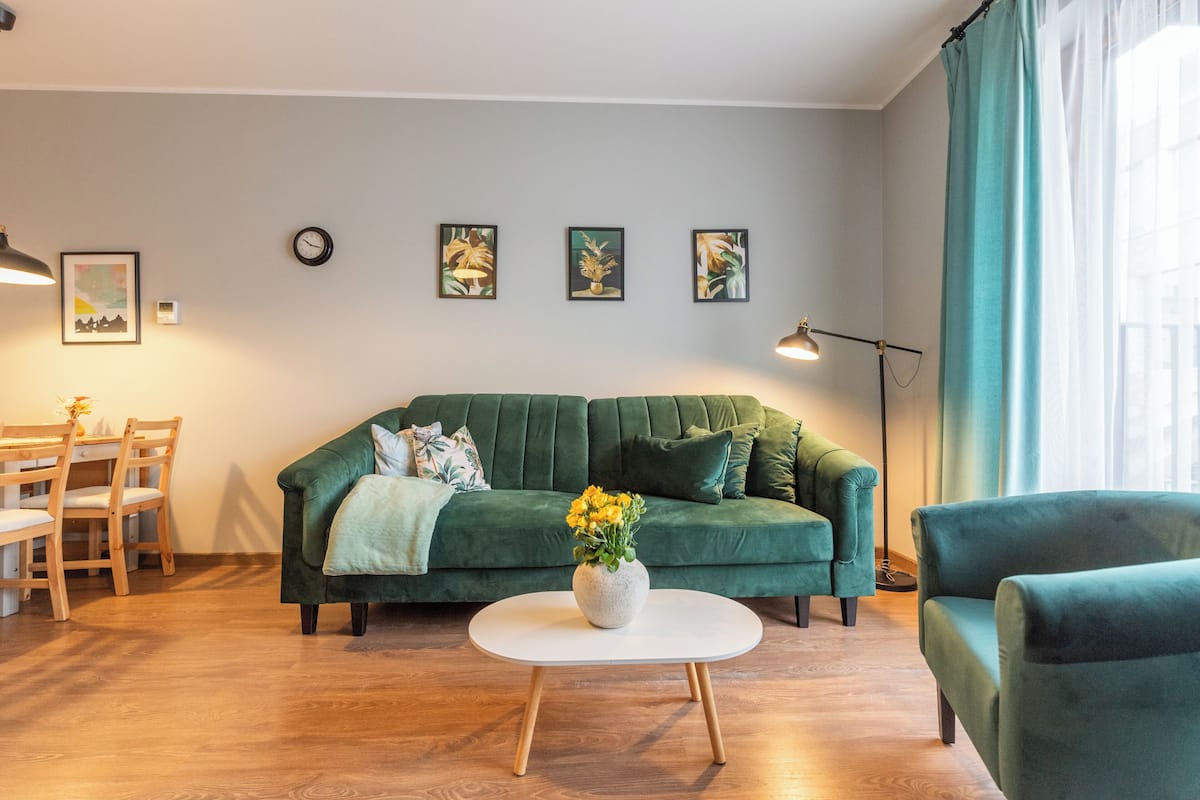 Een groene bank, een witte salontafel, en een eethoek met stoelen en een tafel.