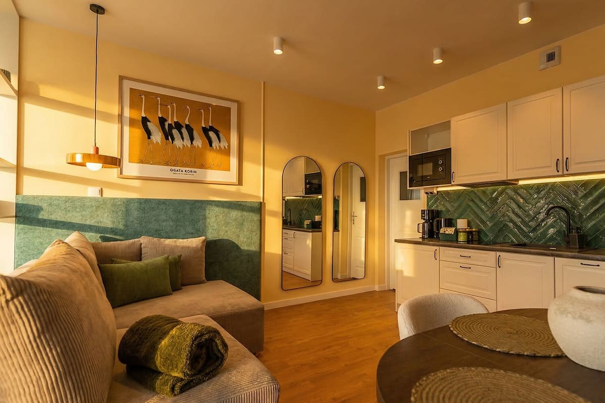 Een moderne woonkamer met een bank, een eettafel en een keuken met witte kasten en een groene spatwand.