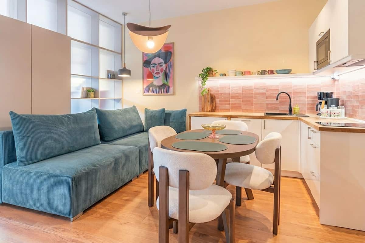 Een moderne woonkamer met een bank, eettafel, stoelen, een hanglamp en een keuken met een spoelbak en aanrecht.
