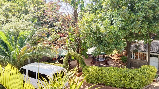 Una camioneta blanca estacionada en un exuberante jardín con zona de patio, rodeada de diversas plantas y árboles.