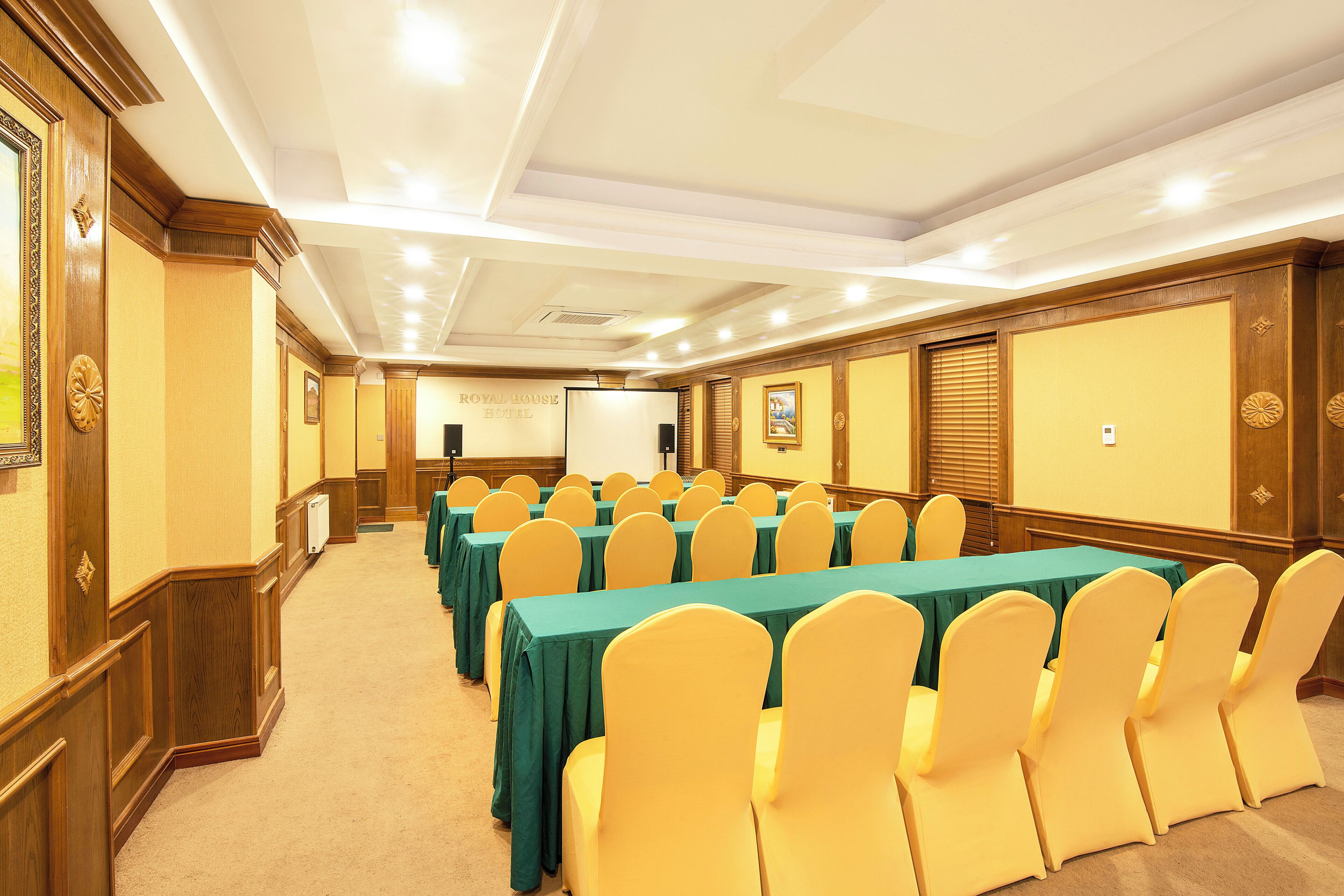 A conference room with rows of tables and chairs, a projector screen, and a sign indicating it's a hotel room.