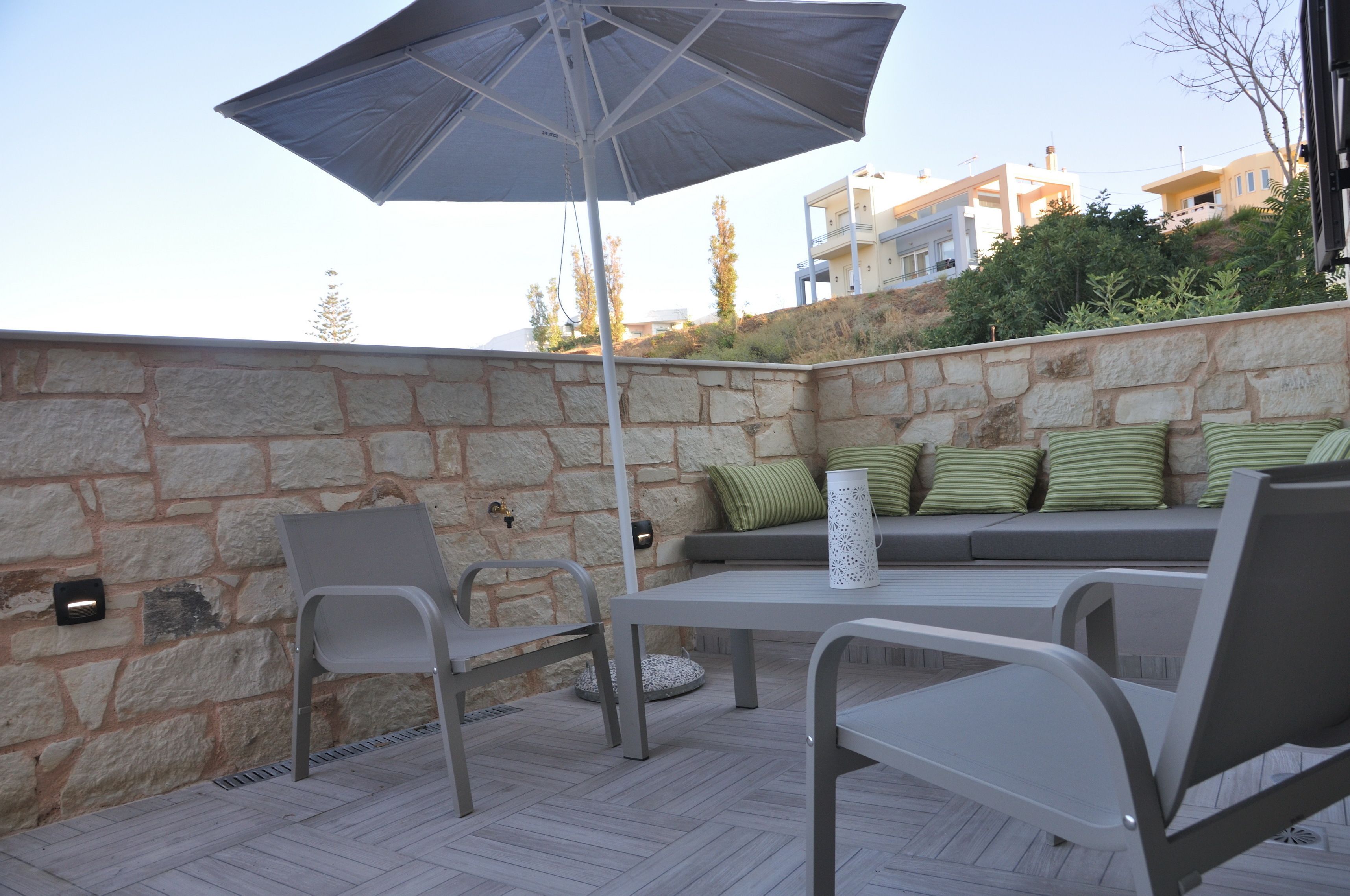 Une terrasse extérieure avec des murs en pierre, un coin salon confortable avec des coussins et une table entourée de chaises.