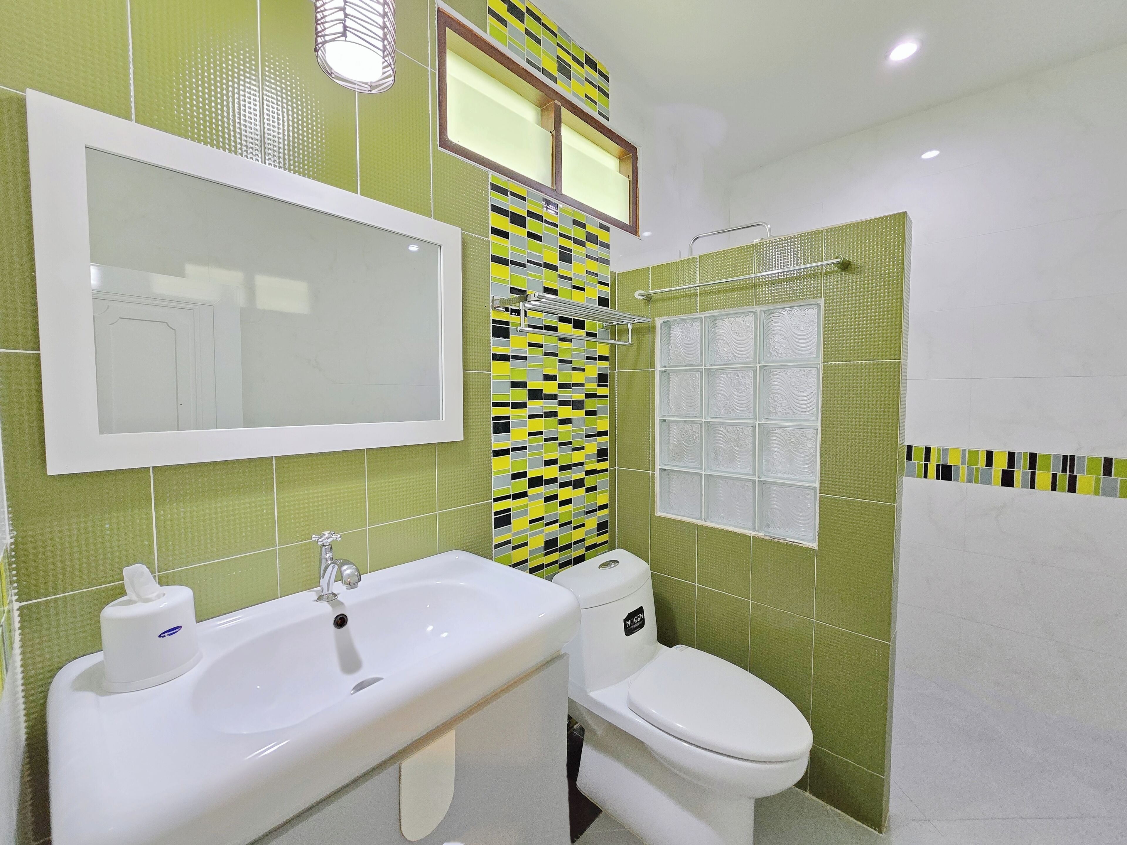 A bathroom with a white sink, a toilet, and a mirror. The walls are tiled with green and yellow patterns.