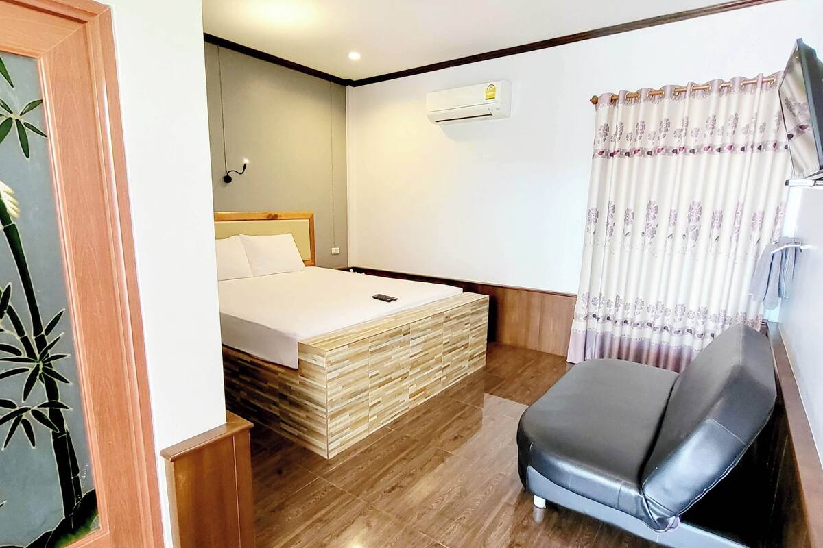 Ein Hotelzimmer mit Bett, Nachttisch, Stuhl, Holzschrank und Klimaanlage.