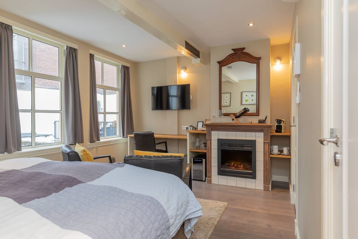 A bedroom with a large bed, a TV, a fireplace, and a desk with a chair.