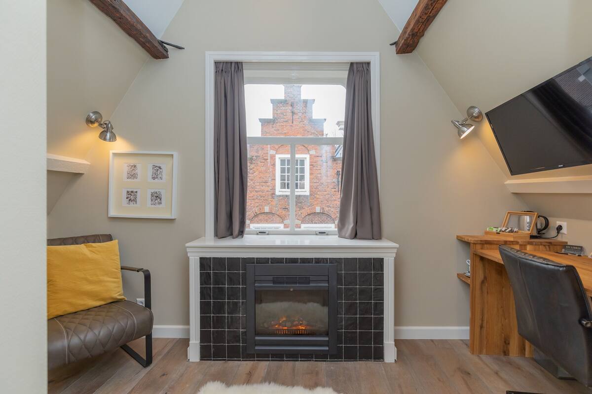 A cozy room with a fireplace, a TV mounted on the wall, and a window with curtains.